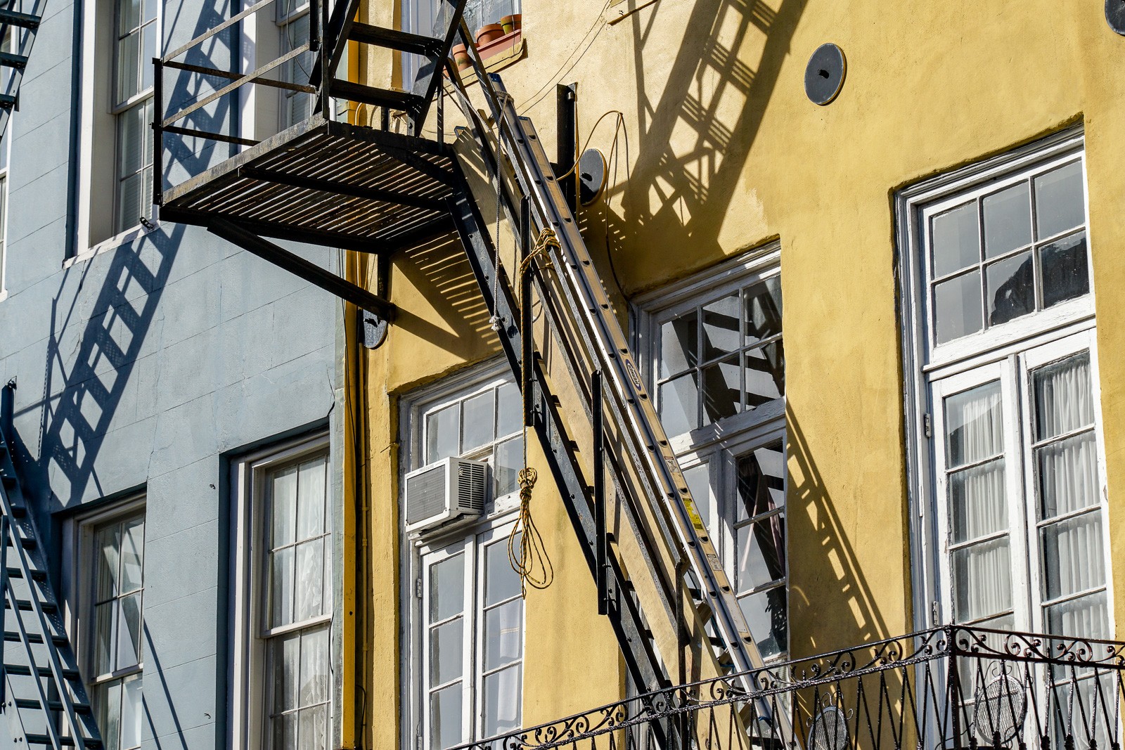 A New Orleans building's ornamental cast-iron balconies and fire escapes rising up a yellow-painted facade, floor by floor in repeating patterns. Decorative and structural at once - as New Orleans tends to be.