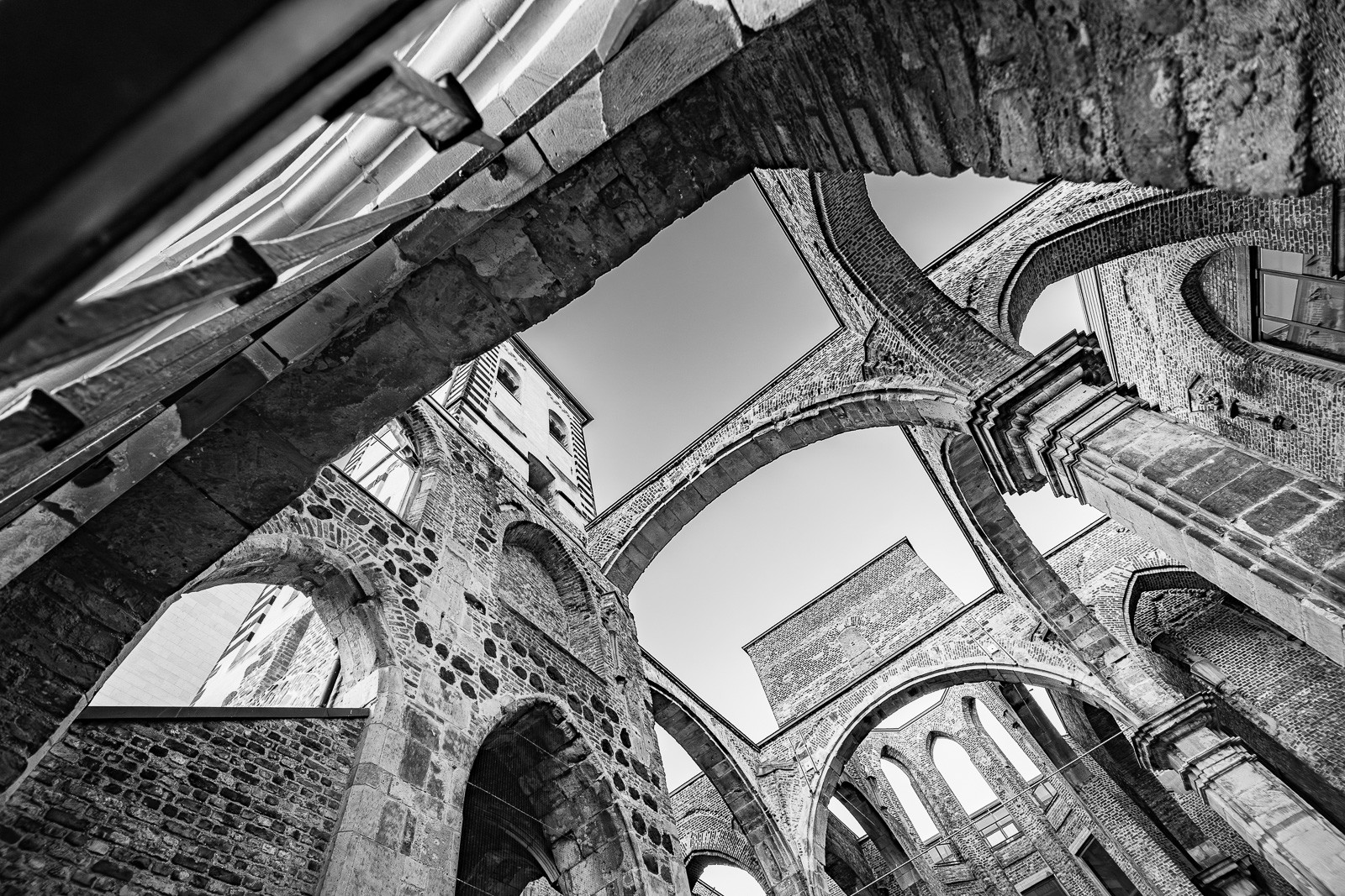 Looking straight up through the roofless nave of Alt St. Alban, Gothic arches and cross-ribs frame the sky that once held the vault. The architecture is defined as much by what is gone as by what remains.