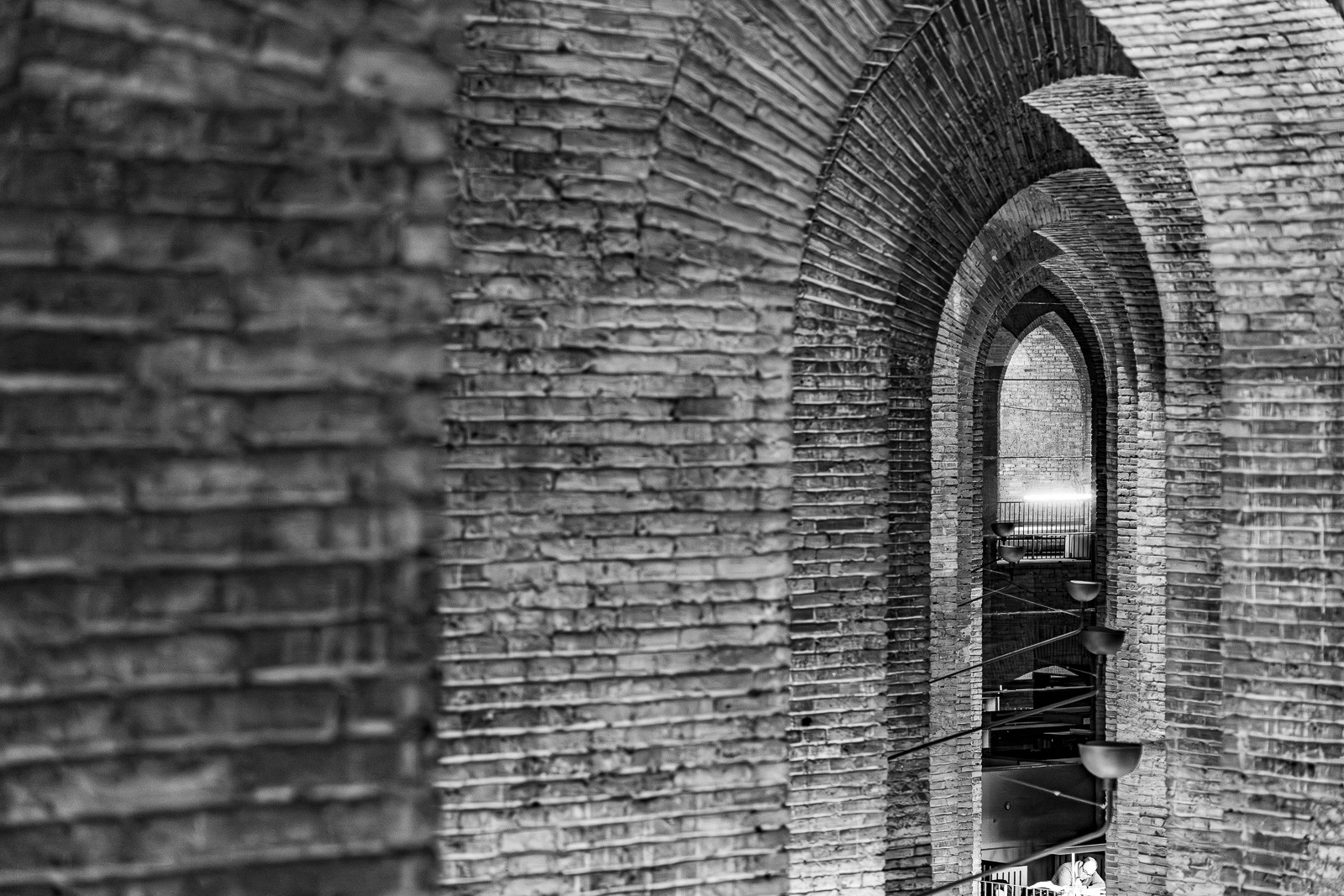A passage in Barcelona with a succession of brick arches overhead, photographed in black and white. Each arch spans the same width