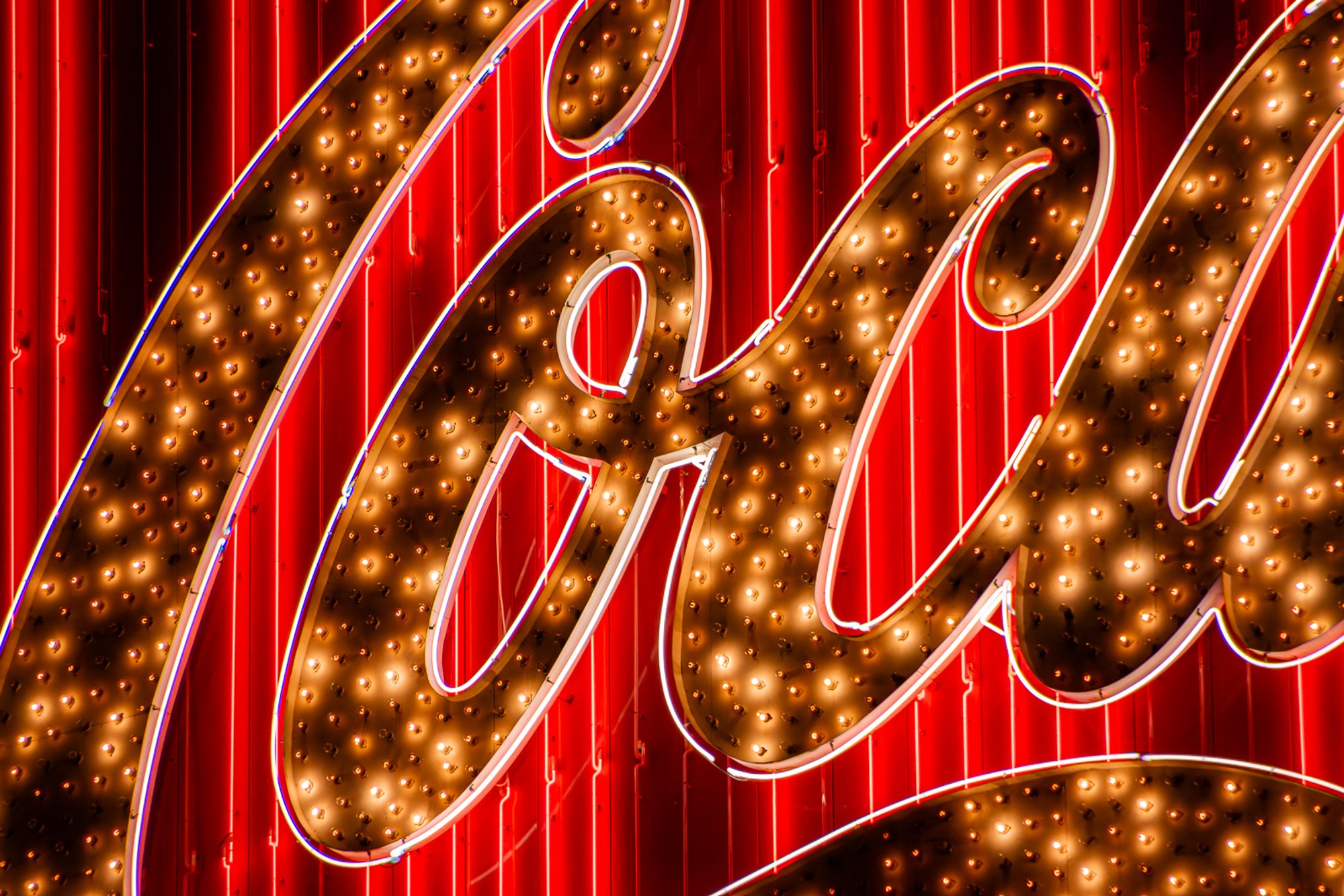 A vintage illuminated sign in San Francisco - the word rendered in large cursive letters outlined in warm bulbs, red neon script behind them. Typography as light source, the letters glowing at the scale of the building they belong to.