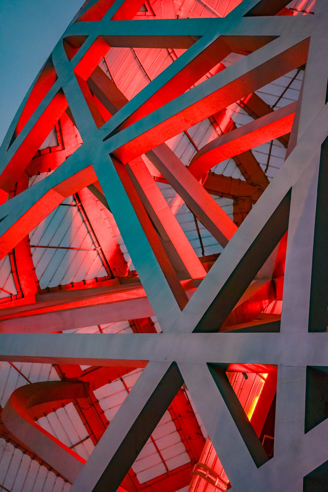 The Beijing National Stadium from outside, its red steel lattice filling the frame. The interlocking beams of Herzog & de Meuron's design create a dense web of diagonals and curves - structure as decoration, or the other way around.
