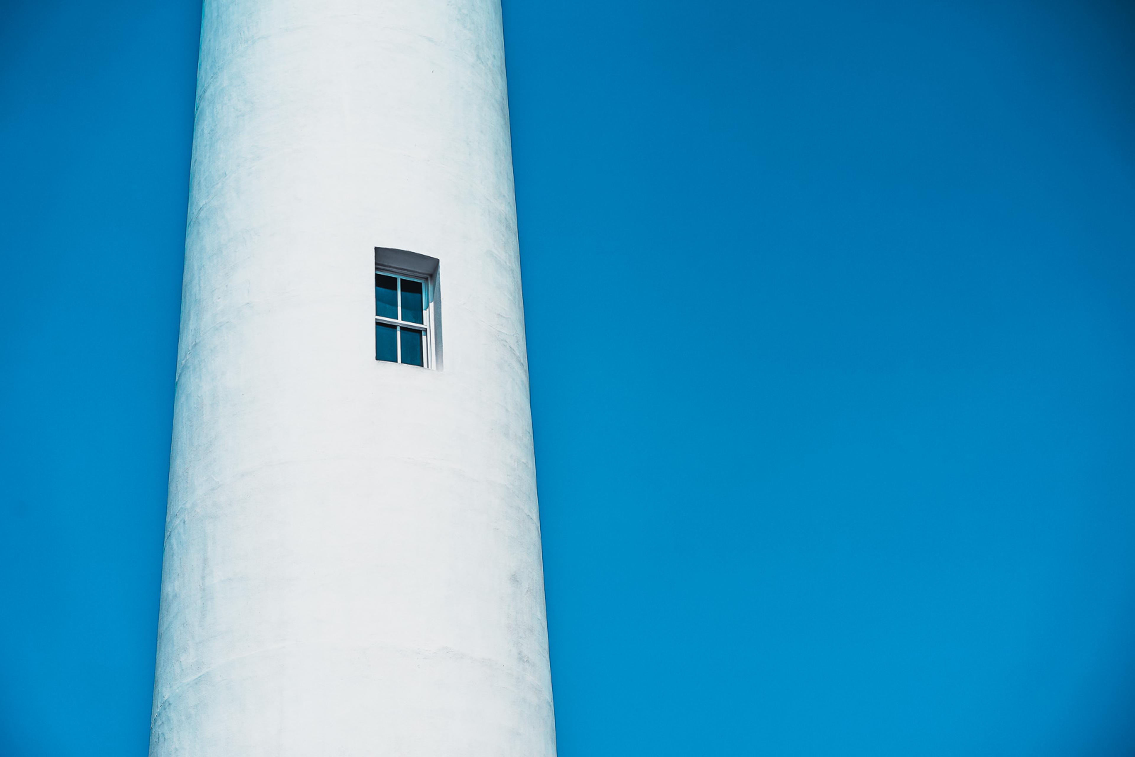 The white cylindrical tower of Pigeon Point Lighthouse against a saturated blue sky, a single small window the only break in the smooth curve. Tower, sky, window - nothing more is needed.