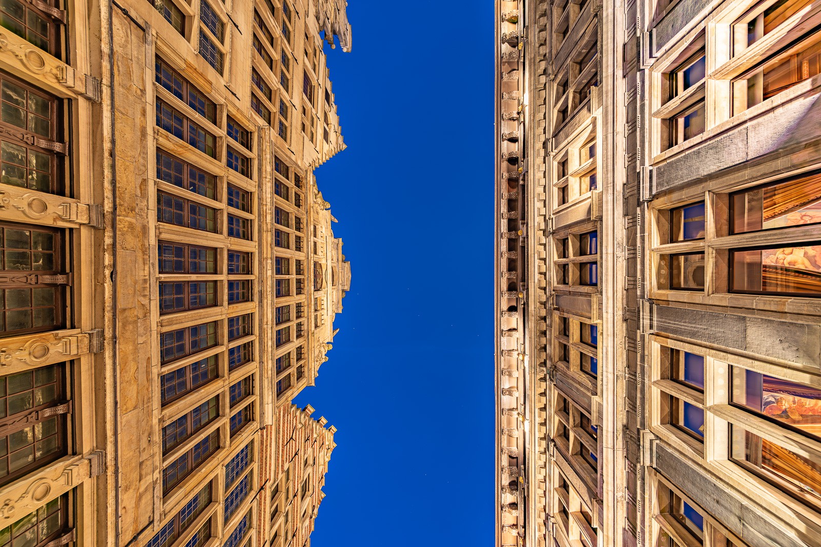 The backside of Antwerp's Renaissance city hall photographed from a low angle in a narrow alleyway, The ornate stonework compressed against a blue narrow strip of an early night sky during magic hour.