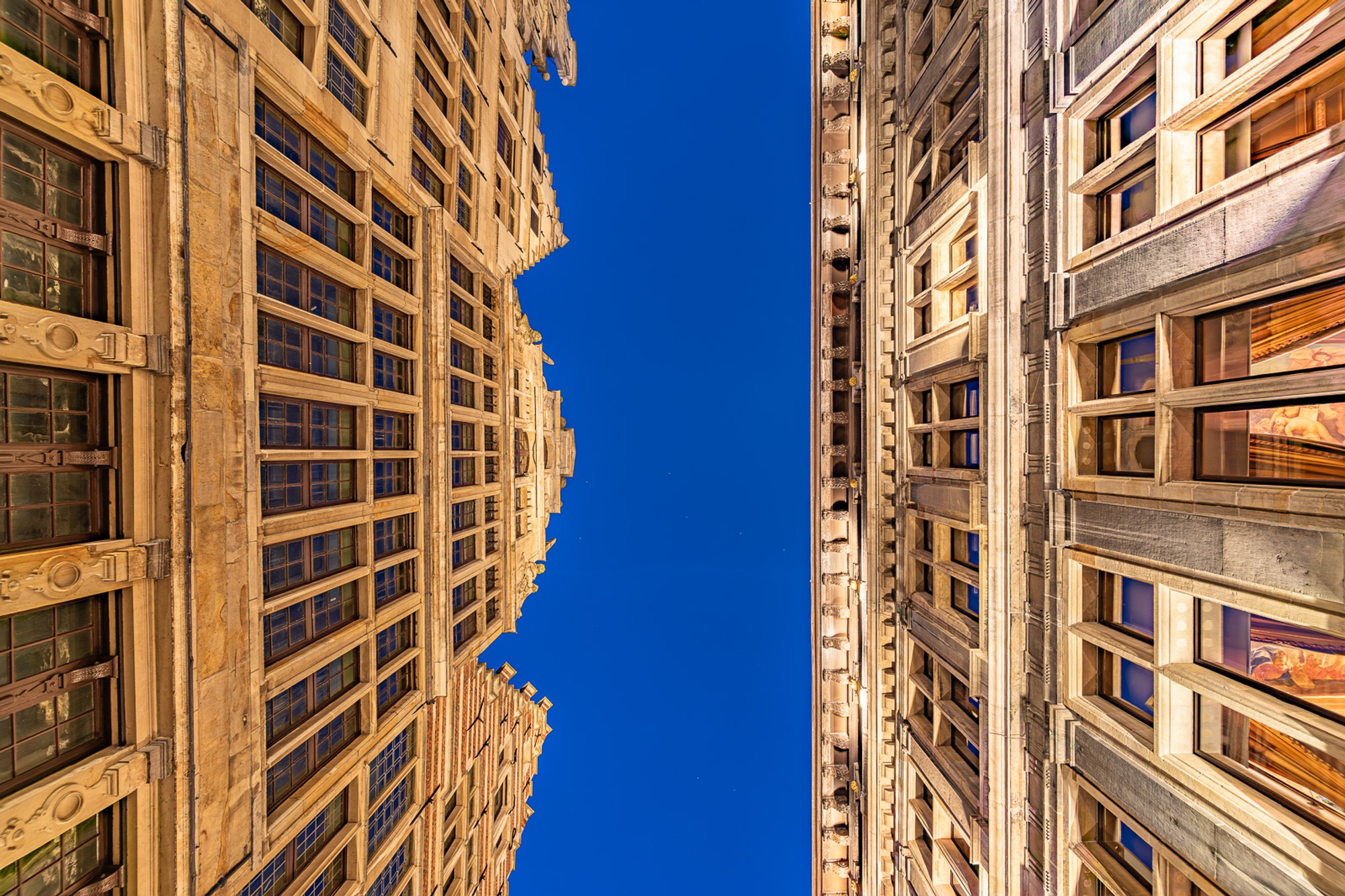The backside of Antwerp's Renaissance city hall photographed from a low angle in a narrow alleyway, The ornate stonework compressed against a blue narrow strip of an early night sky during magic hour.