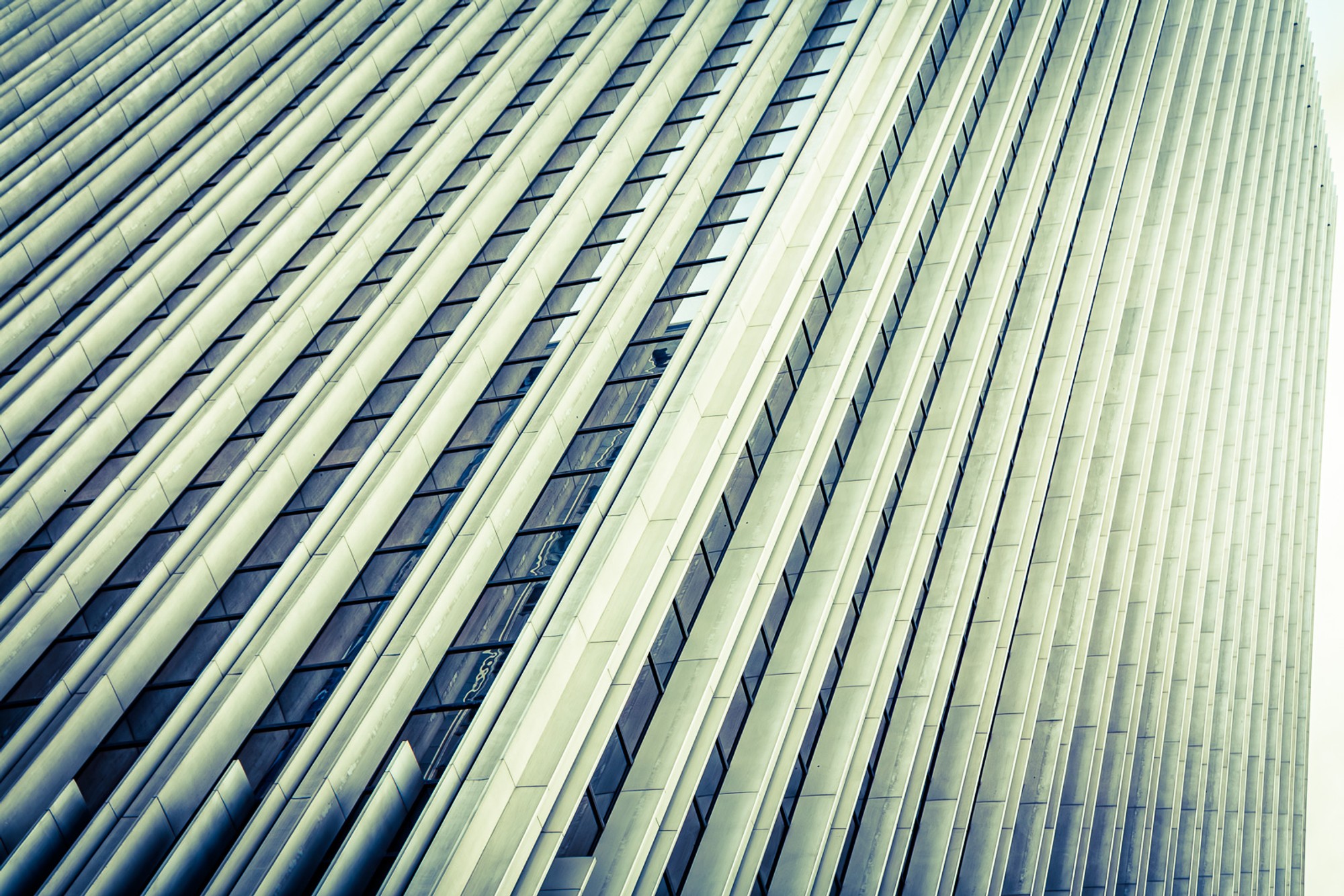 A San Francisco tower seen from street level, its rippled surface creating tonal bands - sky, neighbouring buildings, and street all present simultaneously in the glass. The building is everywhere in the image except where it actually is.