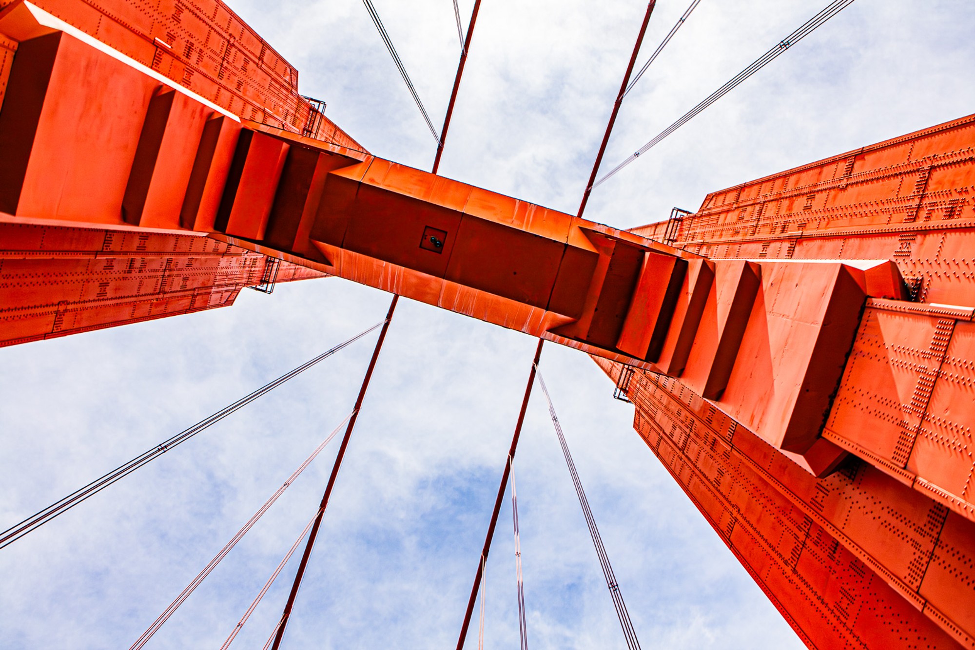 Looking straight up through the Golden Gate Bridge from directly below the roadway, the red steel structure converging symmetrically toward the towers at either end. The view that exists beneath one of the world's most photographed structures.