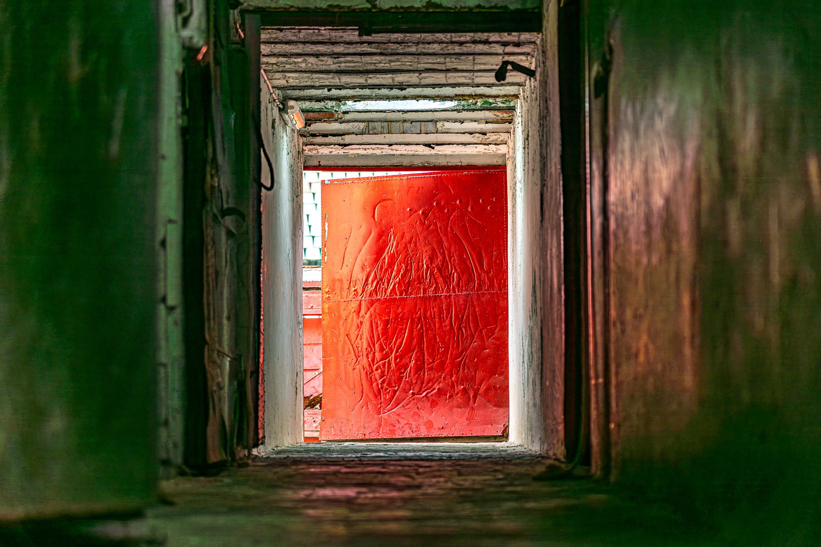 The gateway to La Monumental's sunlit arena, Barcelona's last great bullring. The red door bears the evidence of every entrance — horn strikes traced across the paint in flame-like patterns, each scar a record of something that passed through here.