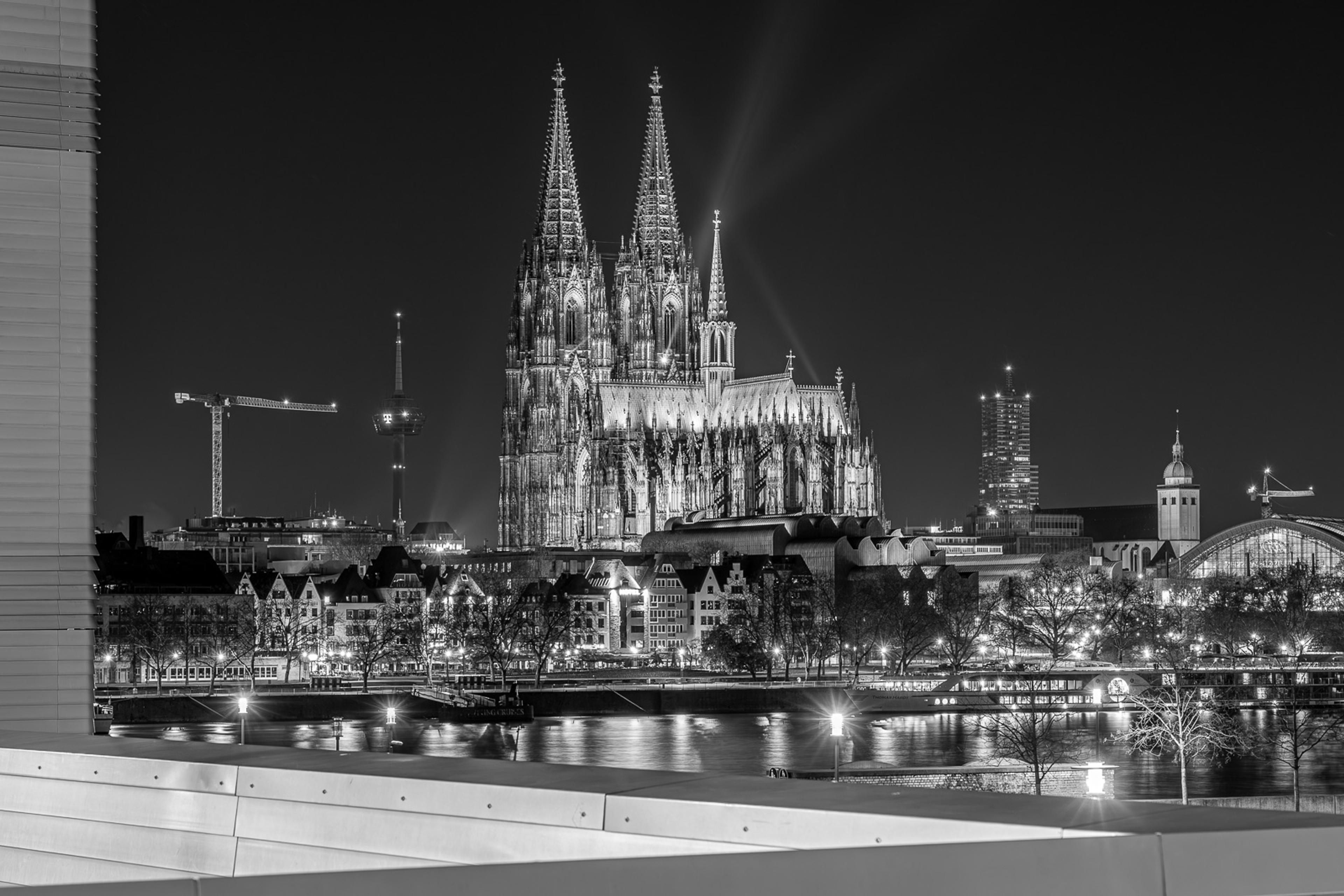 Cologne Cathedral at night, its twin Gothic spires reflected in the Rhine. A long exposure renders the river as dark glass and the city lights as fine streaks along the bank - a view of the cathedral that only exists after midnight.