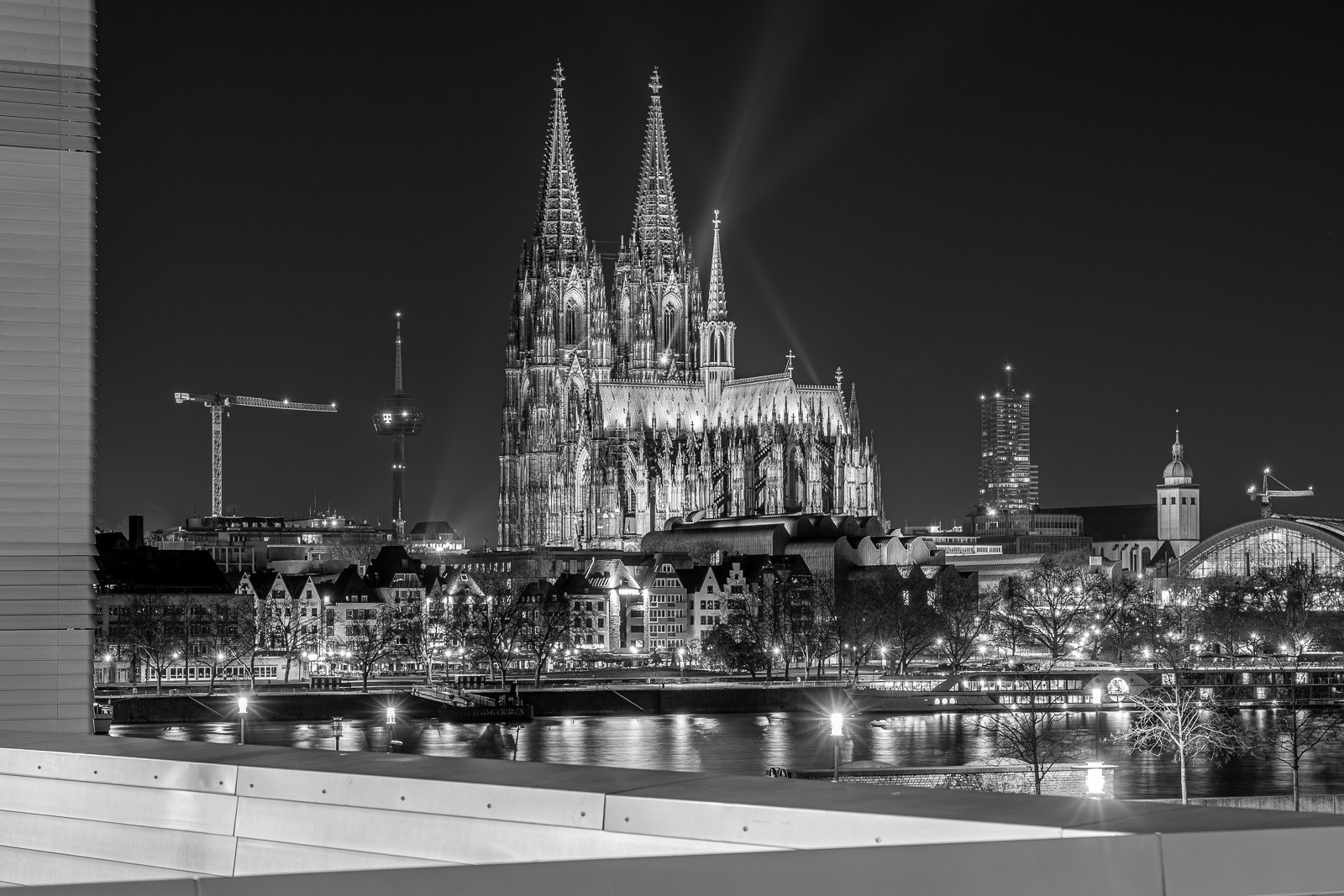 Cologne Cathedral at night, its twin Gothic spires reflected in the Rhine. A long exposure renders the river as dark glass and the city lights as fine streaks along the bank - a view of the cathedral that only exists after midnight.