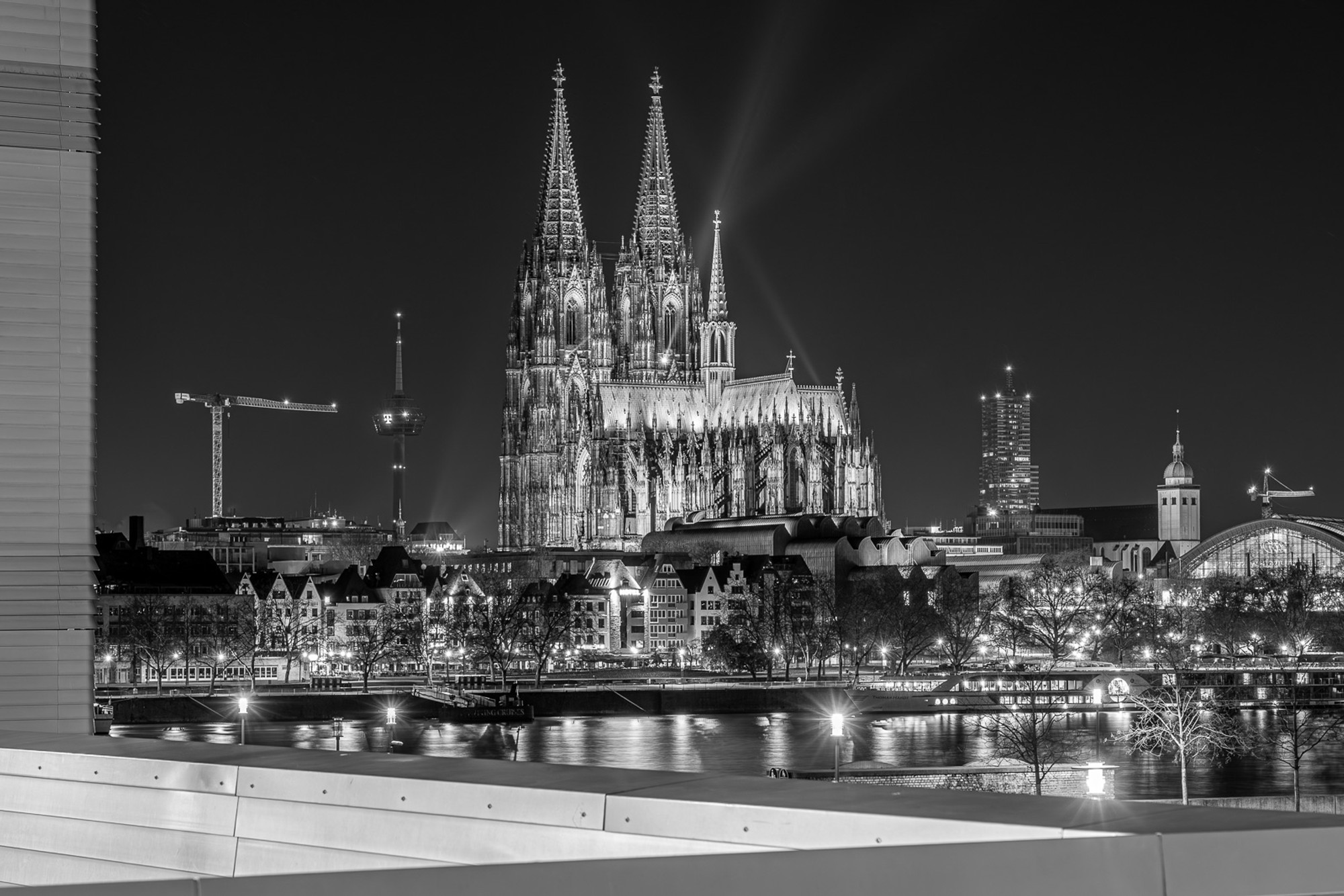 Cologne Cathedral at night, its twin Gothic spires reflected in the Rhine. A long exposure renders the river as dark glass and the city lights as fine streaks along the bank - a view of the cathedral that only exists after midnight.