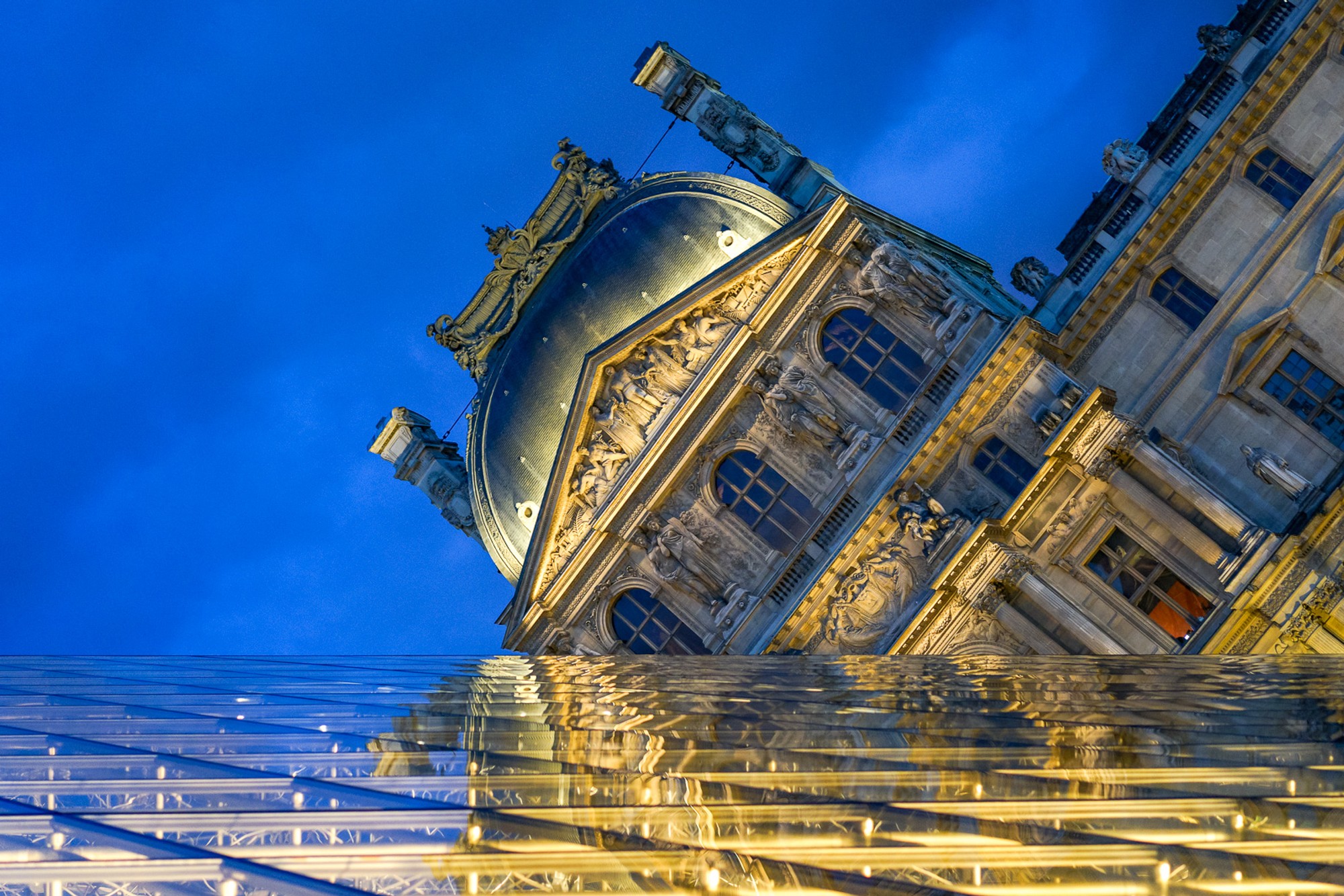 The exterior of the Louvre photographed from a sharp low angle, the classical facade tilting dramatically across the frame. A monument made strange by the angle of approach.
