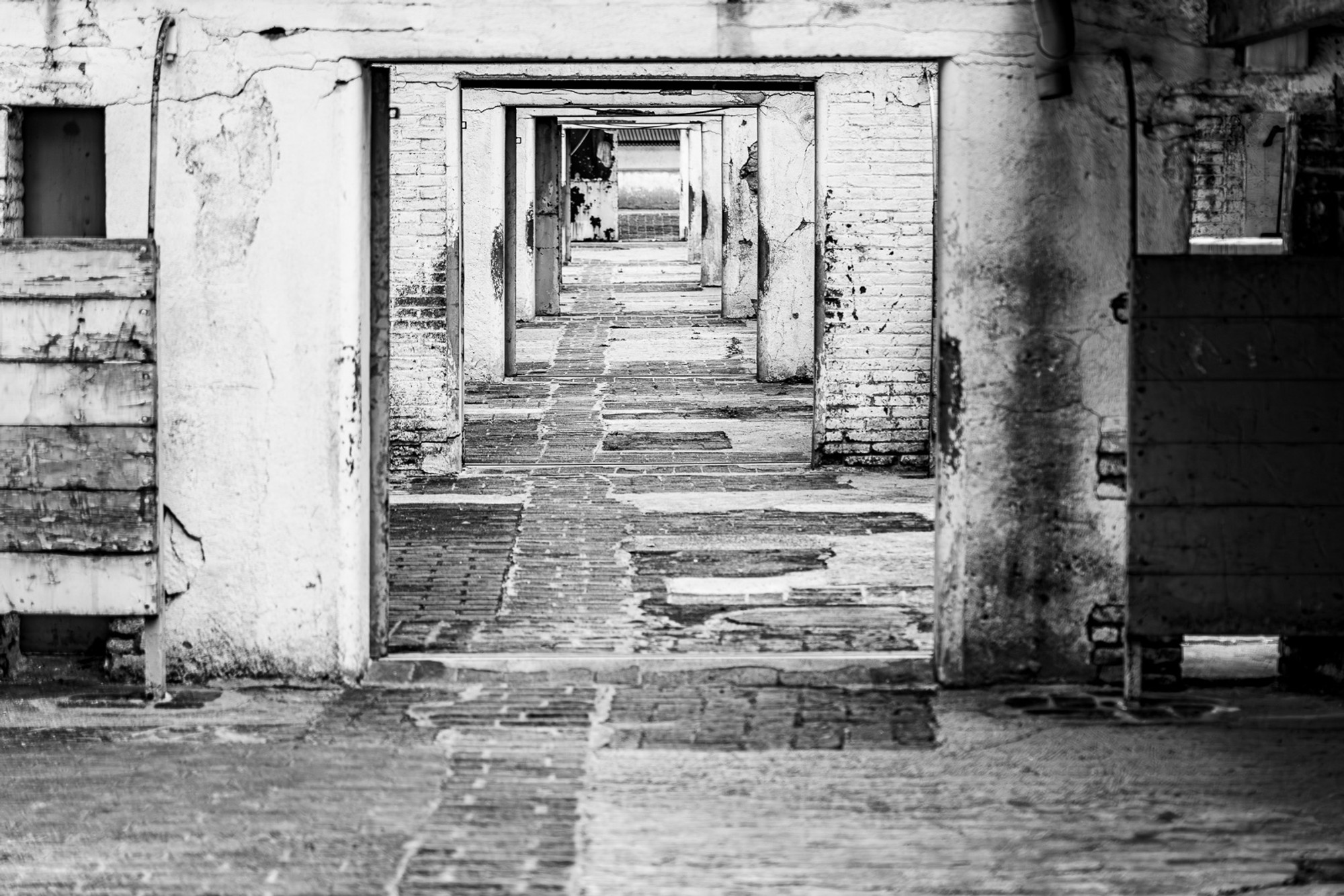 The interior corridors of a Barcelona bullring, in black and white. A sequence of stone arches diminishes in perspective toward a vanishing point of darkness - repetition and shadow doing exactly what great architecture can do.
