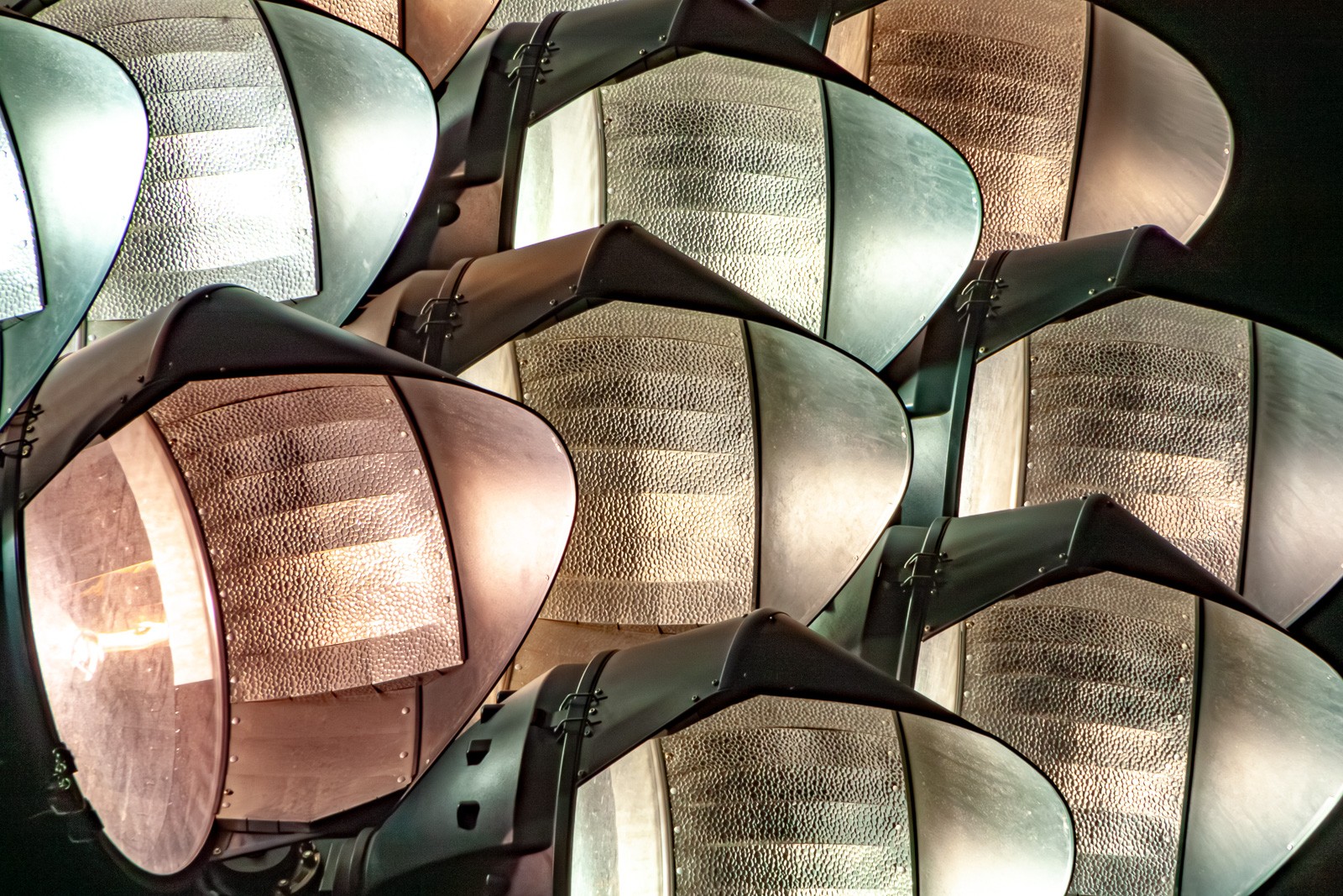 Stadium floodlight fixtures at Stanford photographed from below at dusk, their concave reflector dishes pointing in slightly different directions. The engineering of spectacle, seen before the spectacle begins.