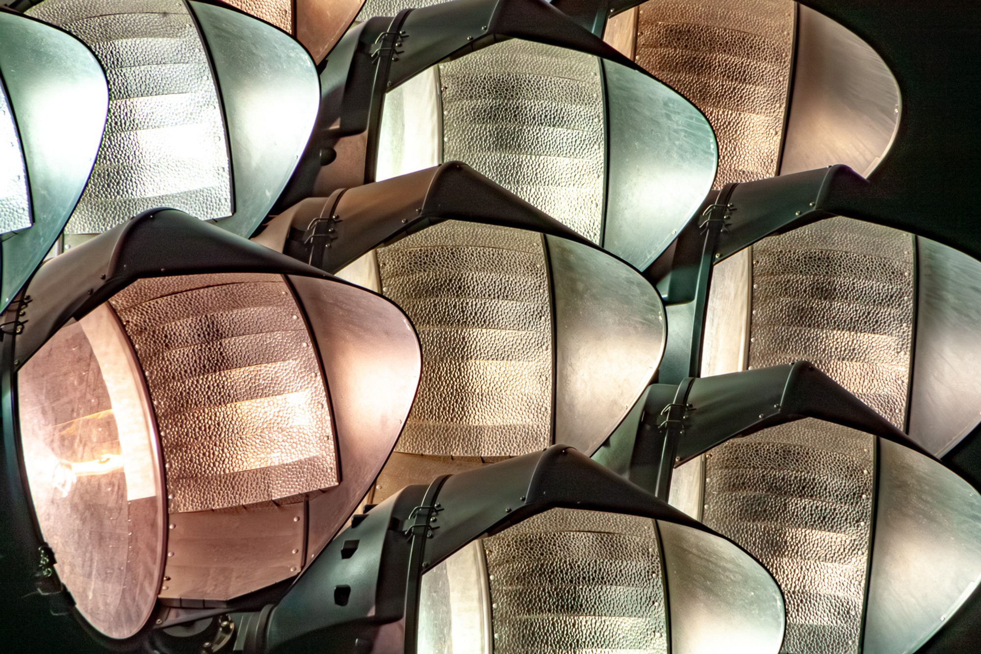 Stadium floodlight fixtures at Stanford photographed from below at dusk, their concave reflector dishes pointing in slightly different directions. The engineering of spectacle, seen before the spectacle begins.
