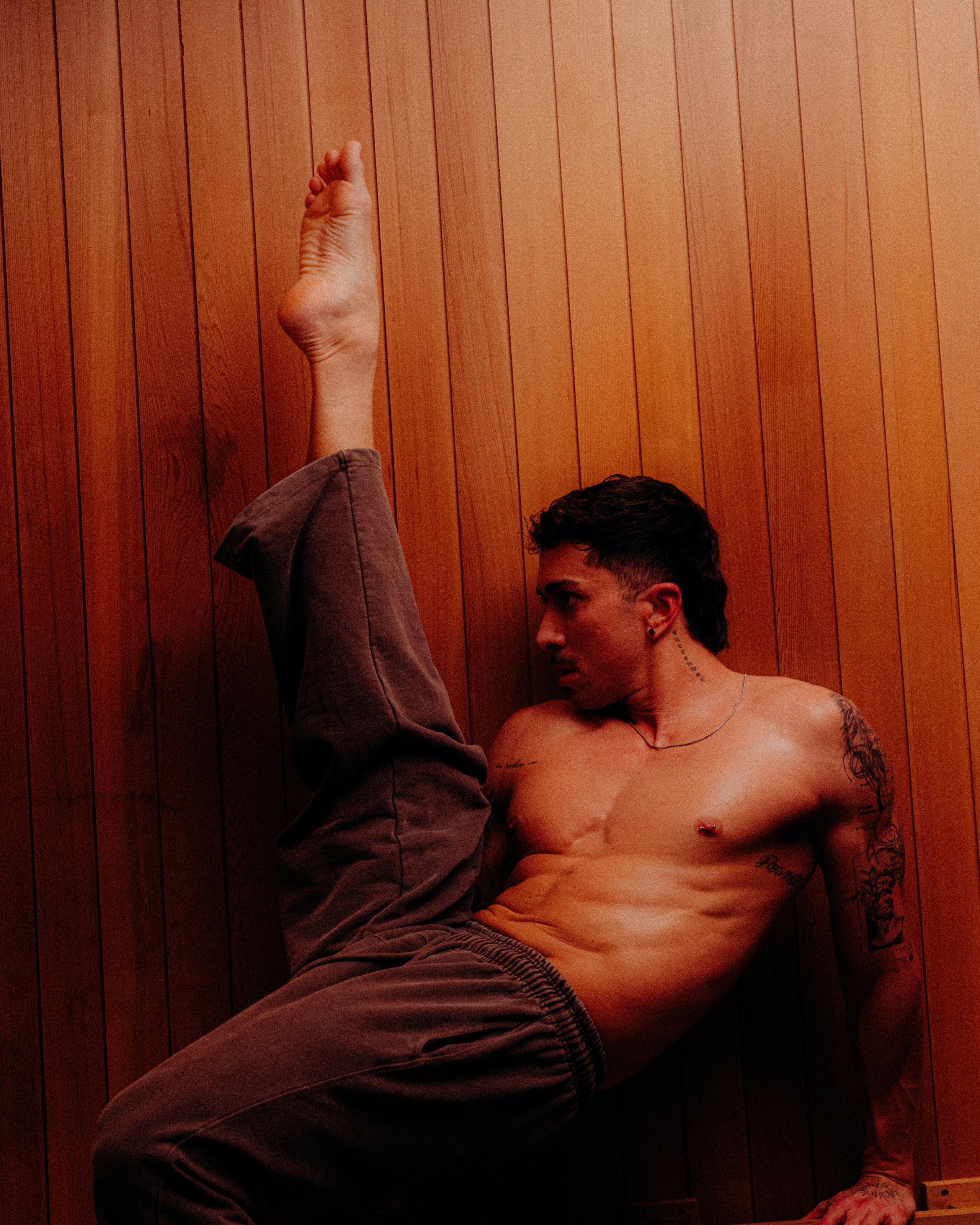 Guest reclining against a wood sauna wall with one arm raised.