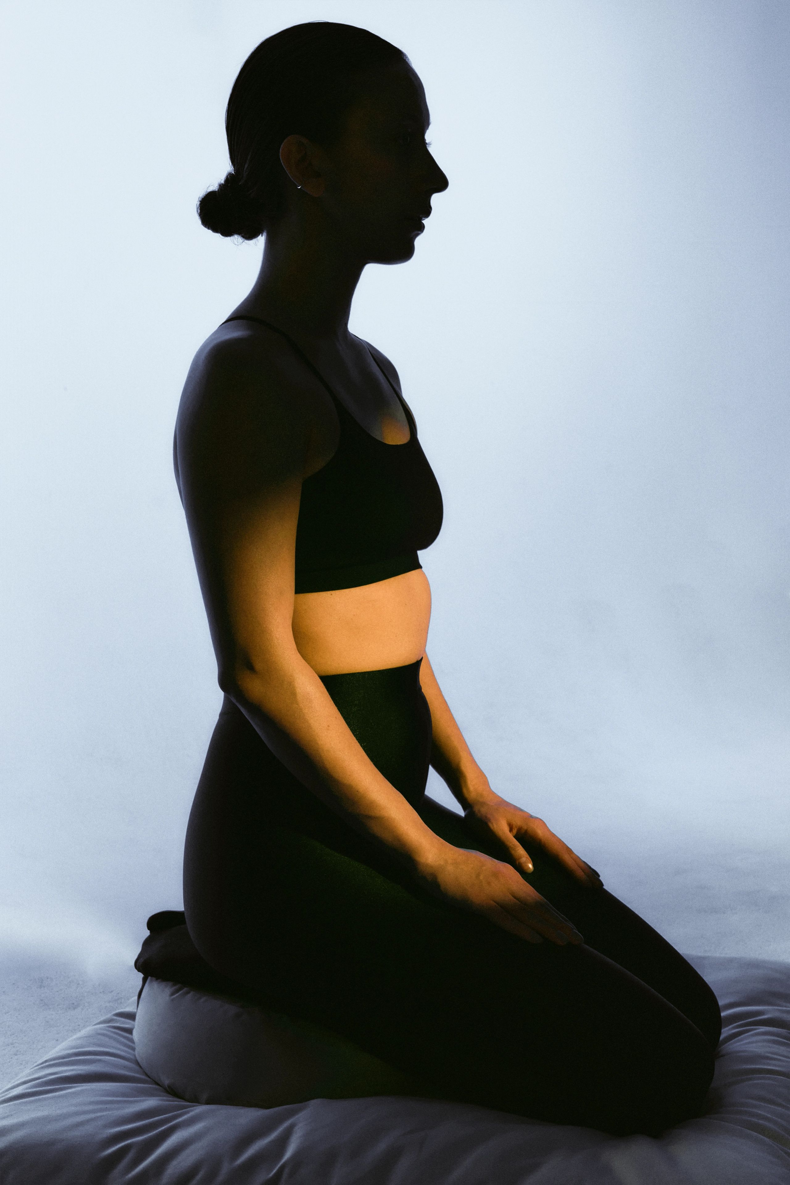 Seated figure in profile against a softly lit blue background.
