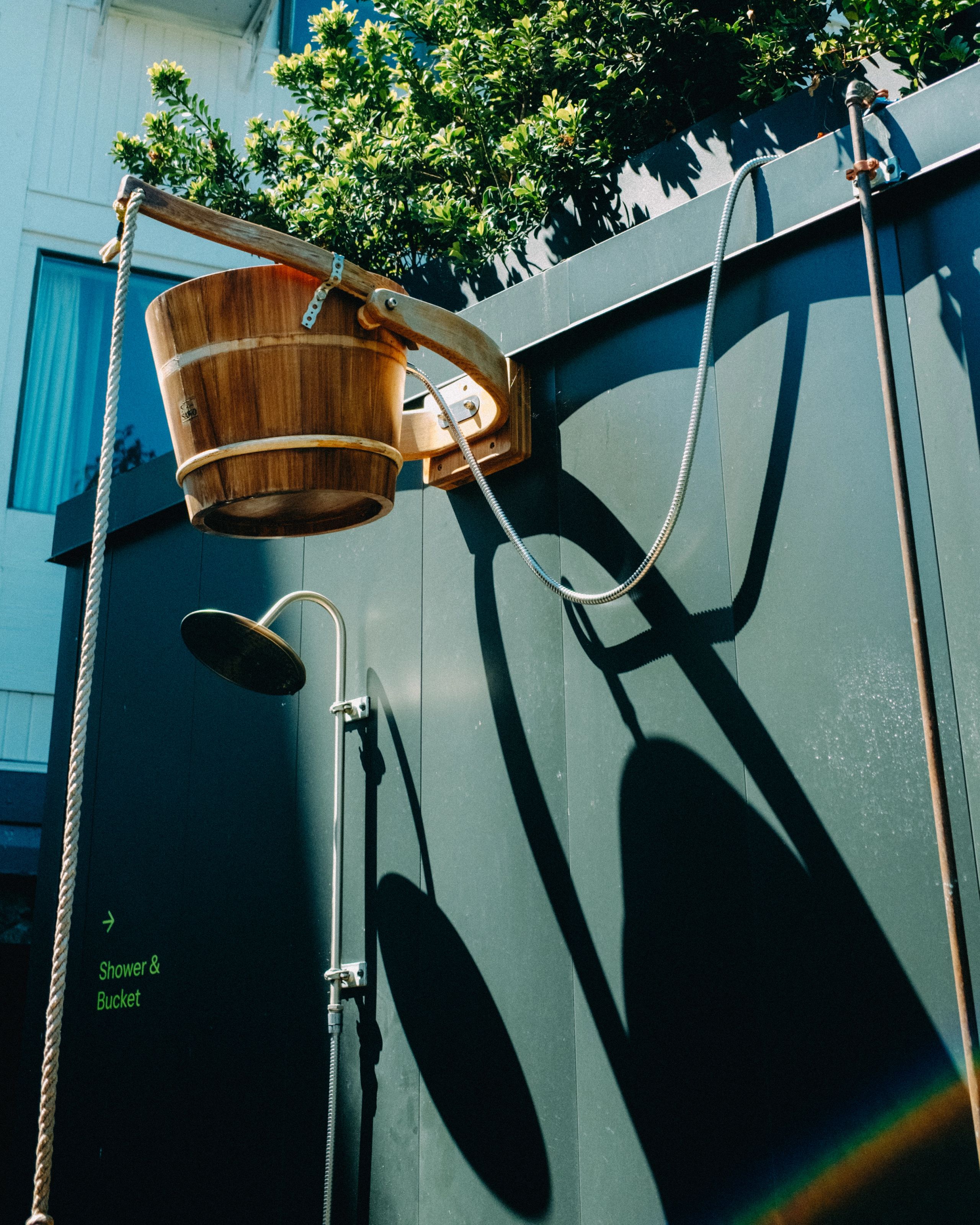 Wooden bucket shower against a blue wall at Aerth.