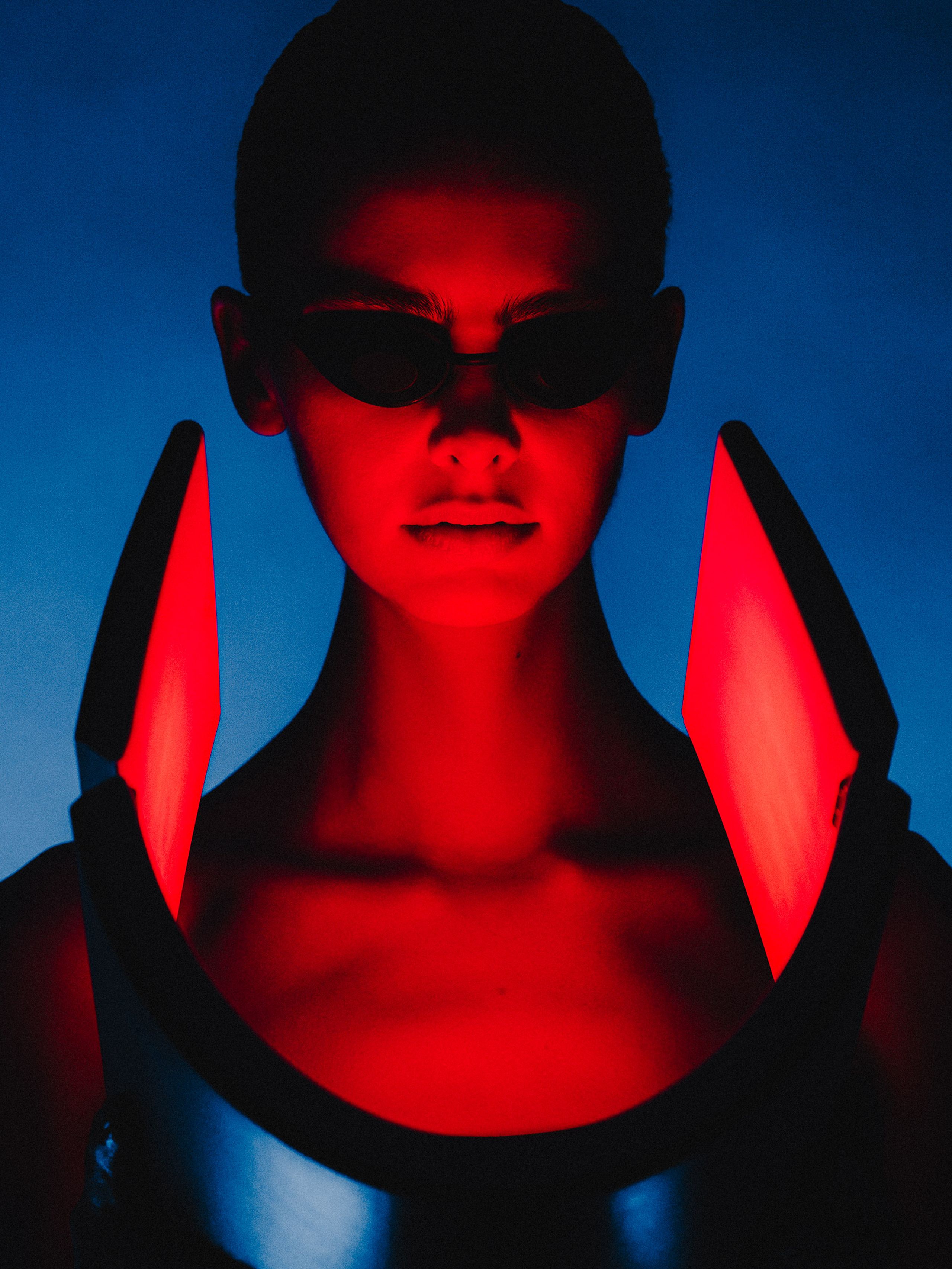 Portrait in blue light with red illuminated panels framing the face.