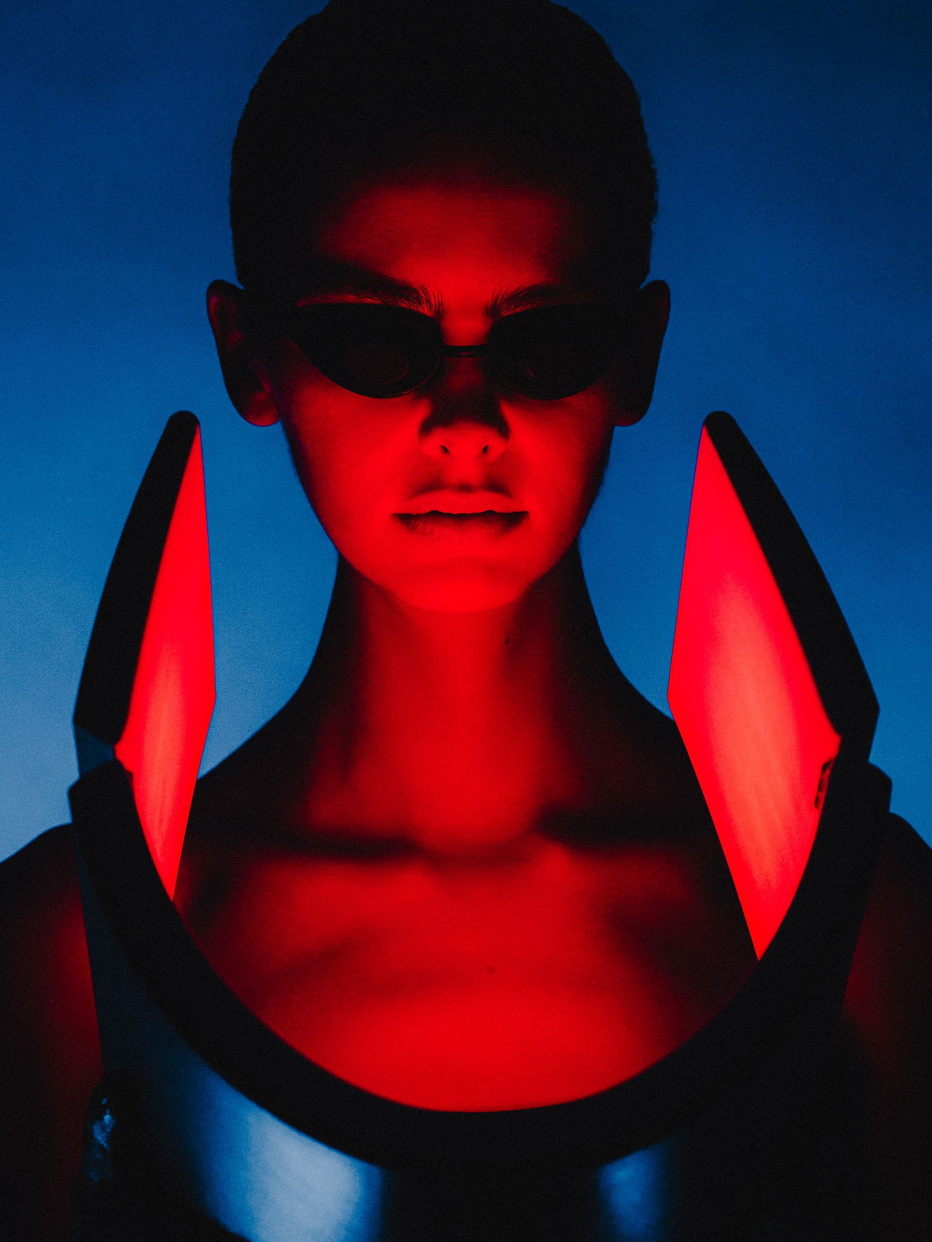 Portrait in blue light with red illuminated panels framing the face.