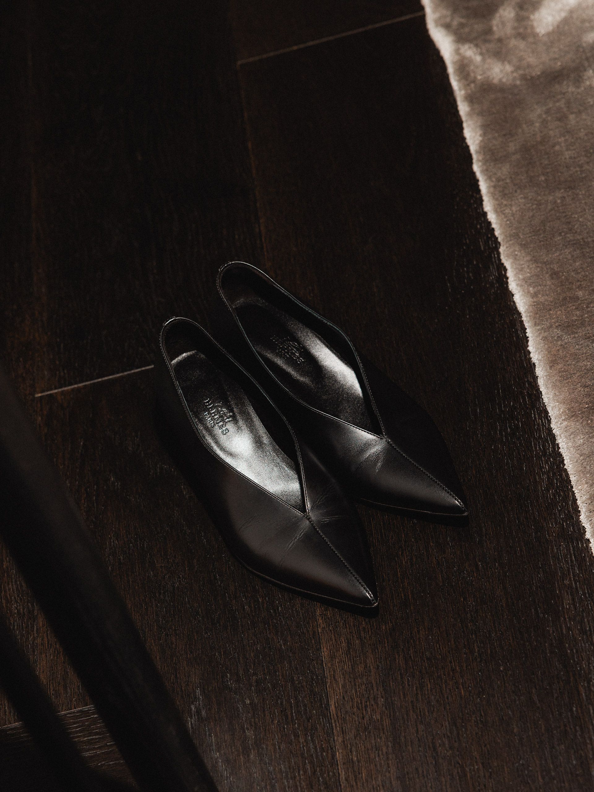 Black pointed shoes resting on a dark wood floor.
