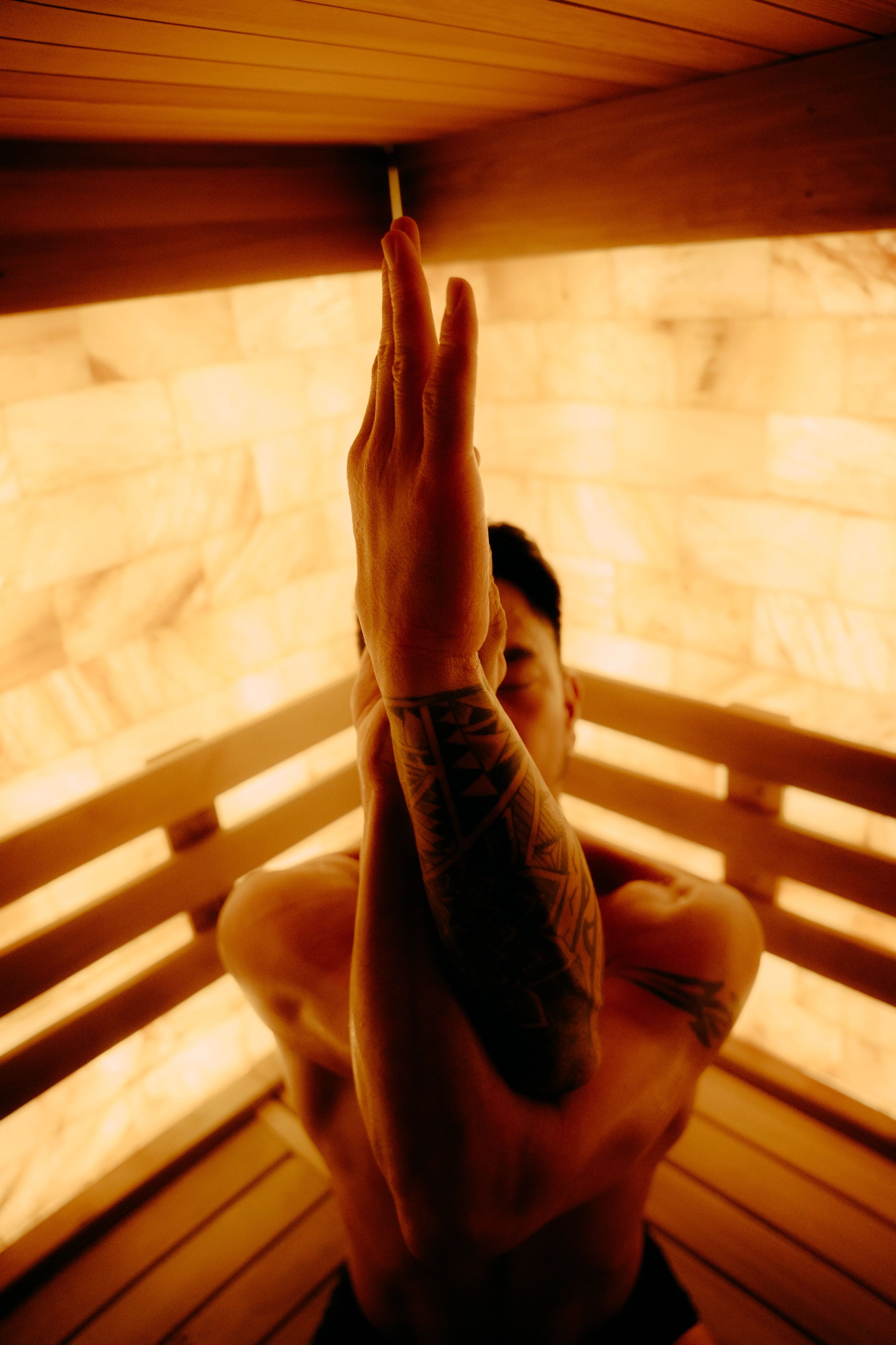 Guest stretching in a warmly lit wood sauna at AetherHaus.