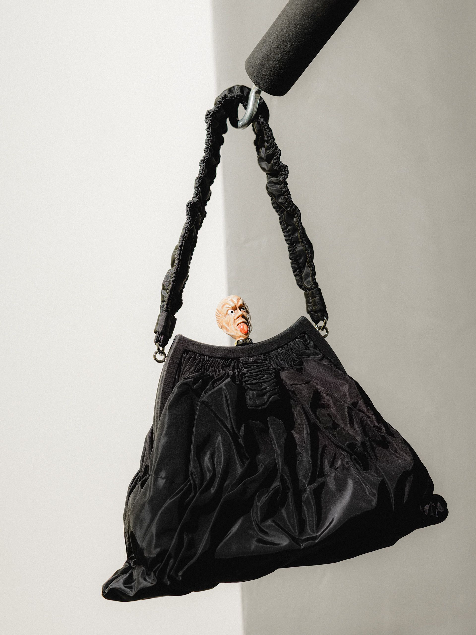 Black gathered handbag suspended against a pale background.