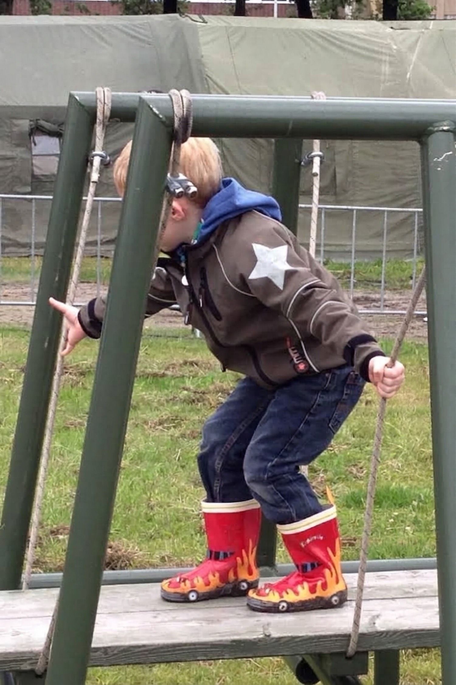 A young boy in red flame wellies climbing a playground frame.