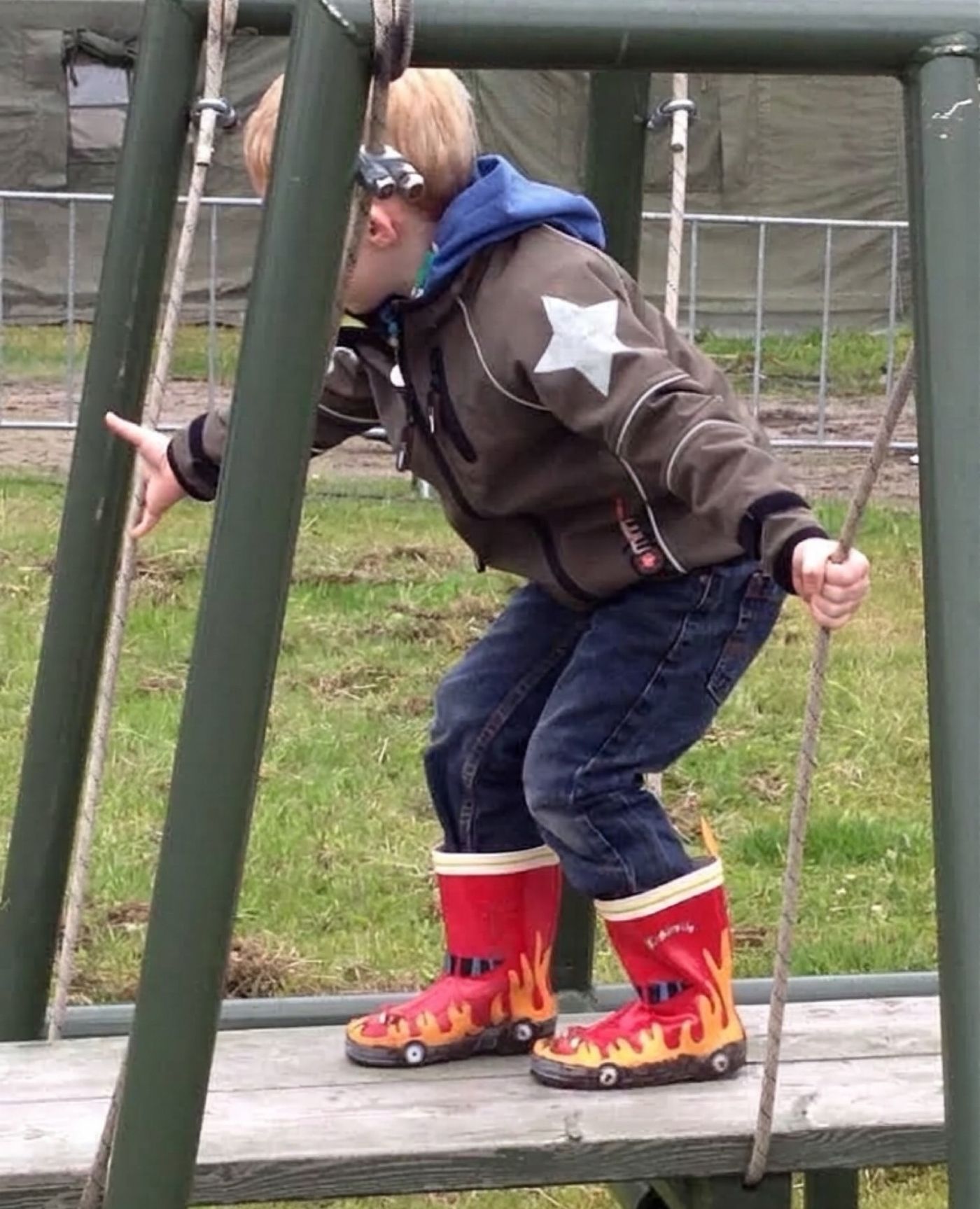 My young son in red flame wellies climbing a playground frame.