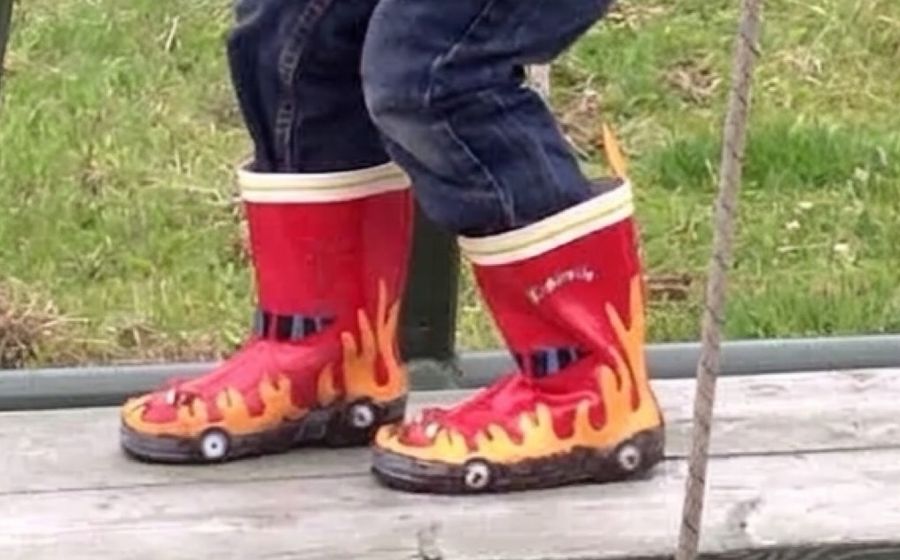 A young boy in red flame wellies climbing a playground frame.