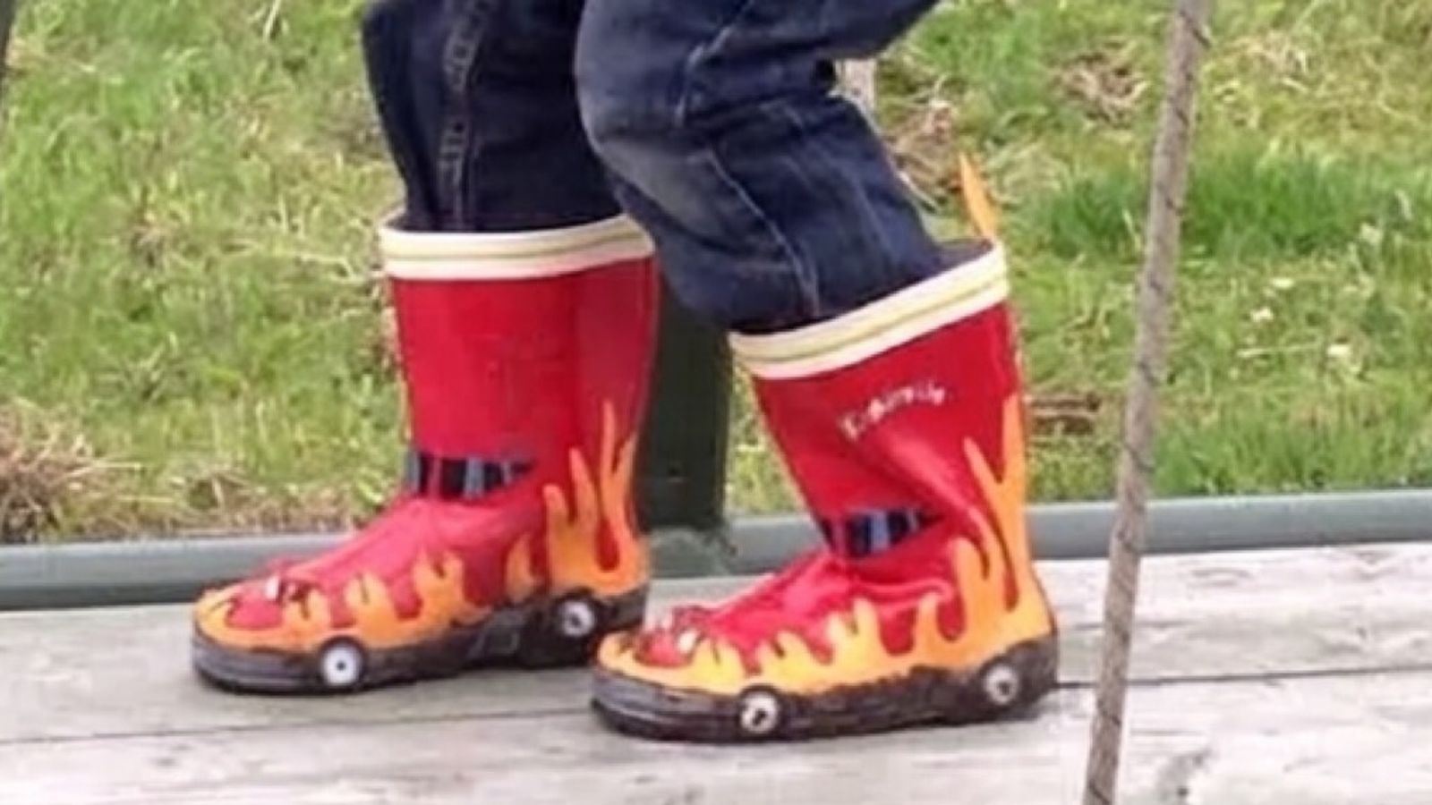 A young boy in red flame wellies climbing a playground frame.
