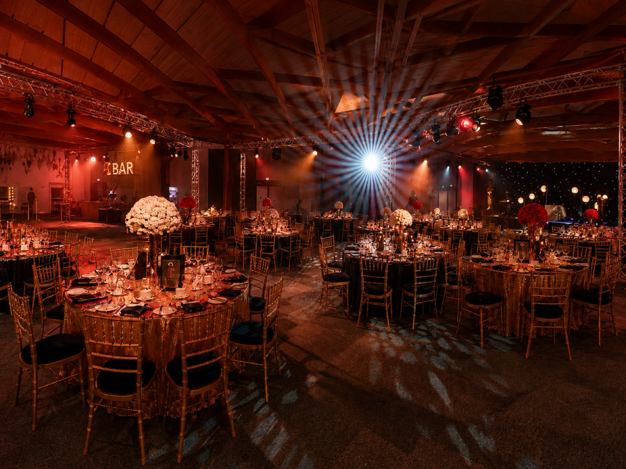An elegant gala dinner setting with gold tables, dramatic red lighting and striking stage effects creating an immersive event atmosphere