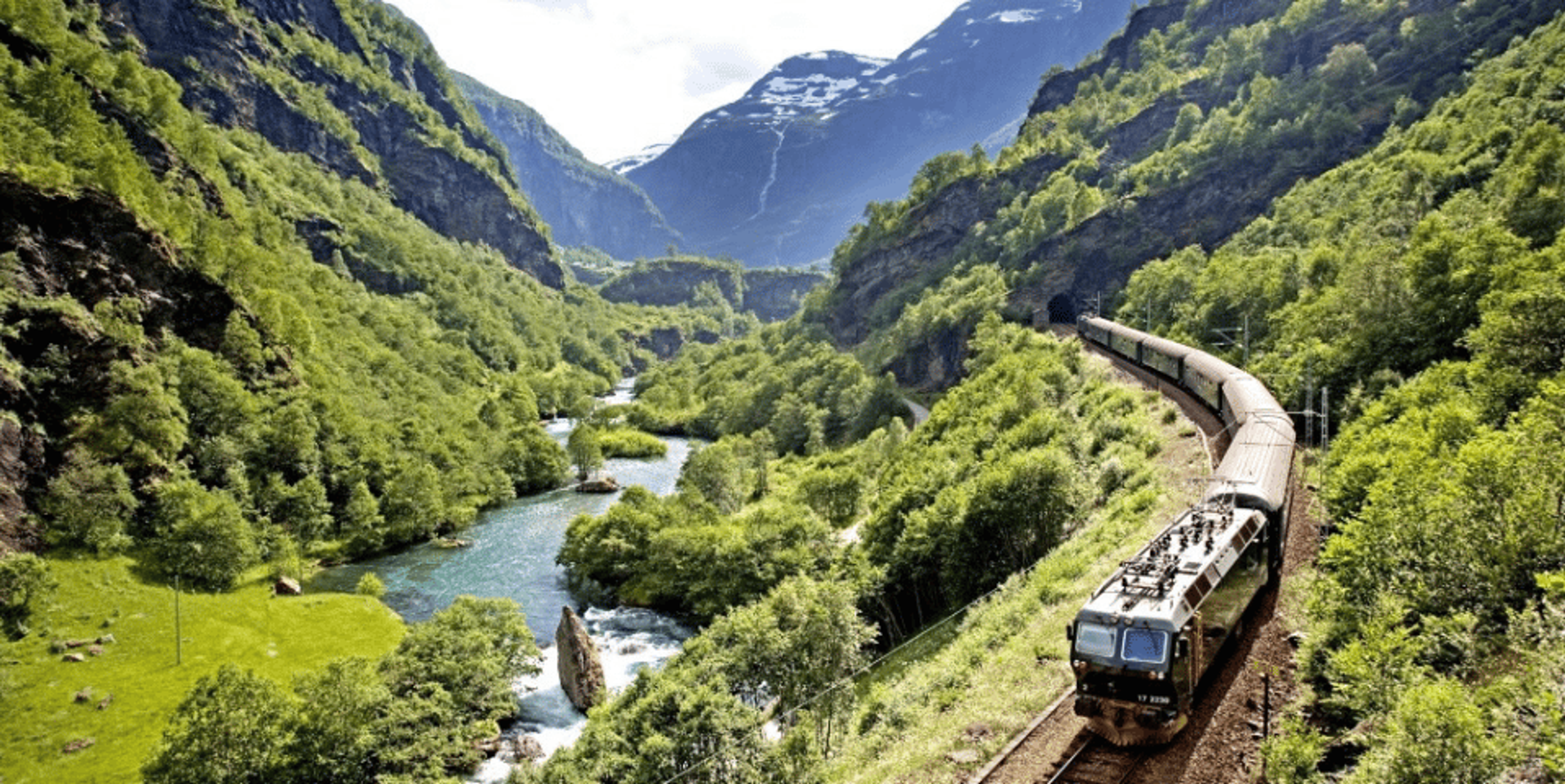 A train coursing through green mountains with a nearby river