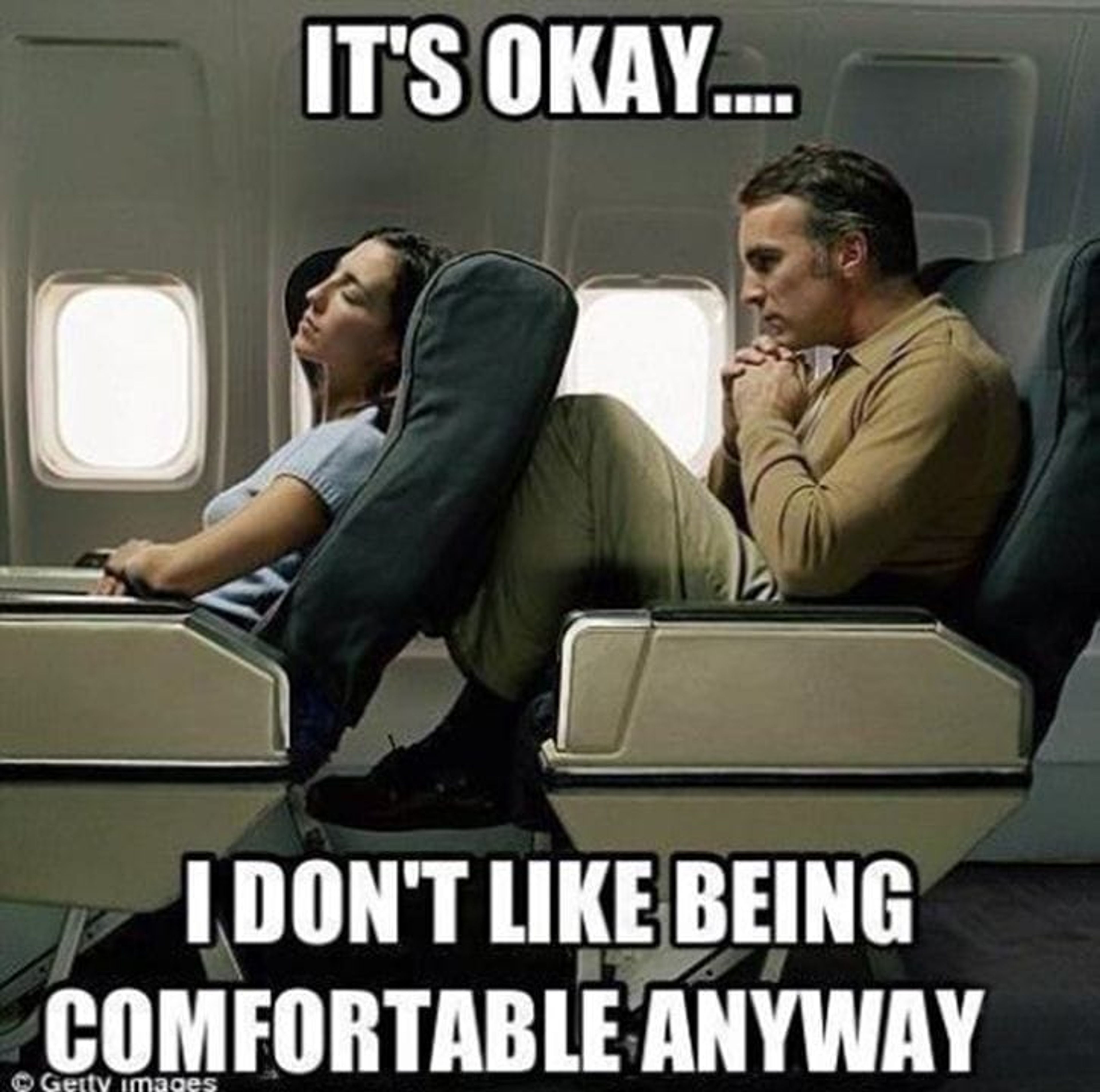A man sitting scrunched up in an econom seat with the seat in front of him reclined