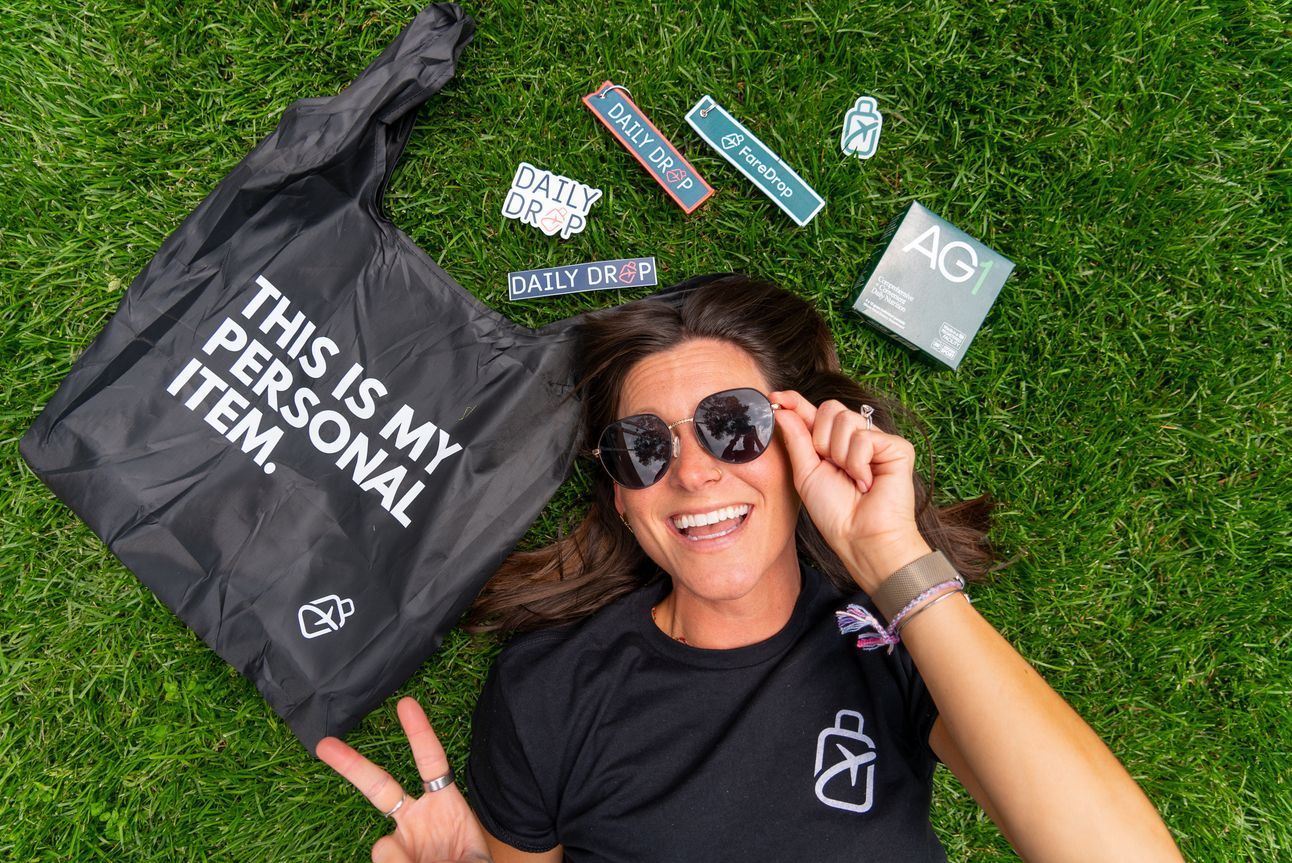 Kara lying in the grass with a tote, stickers, and bag tags