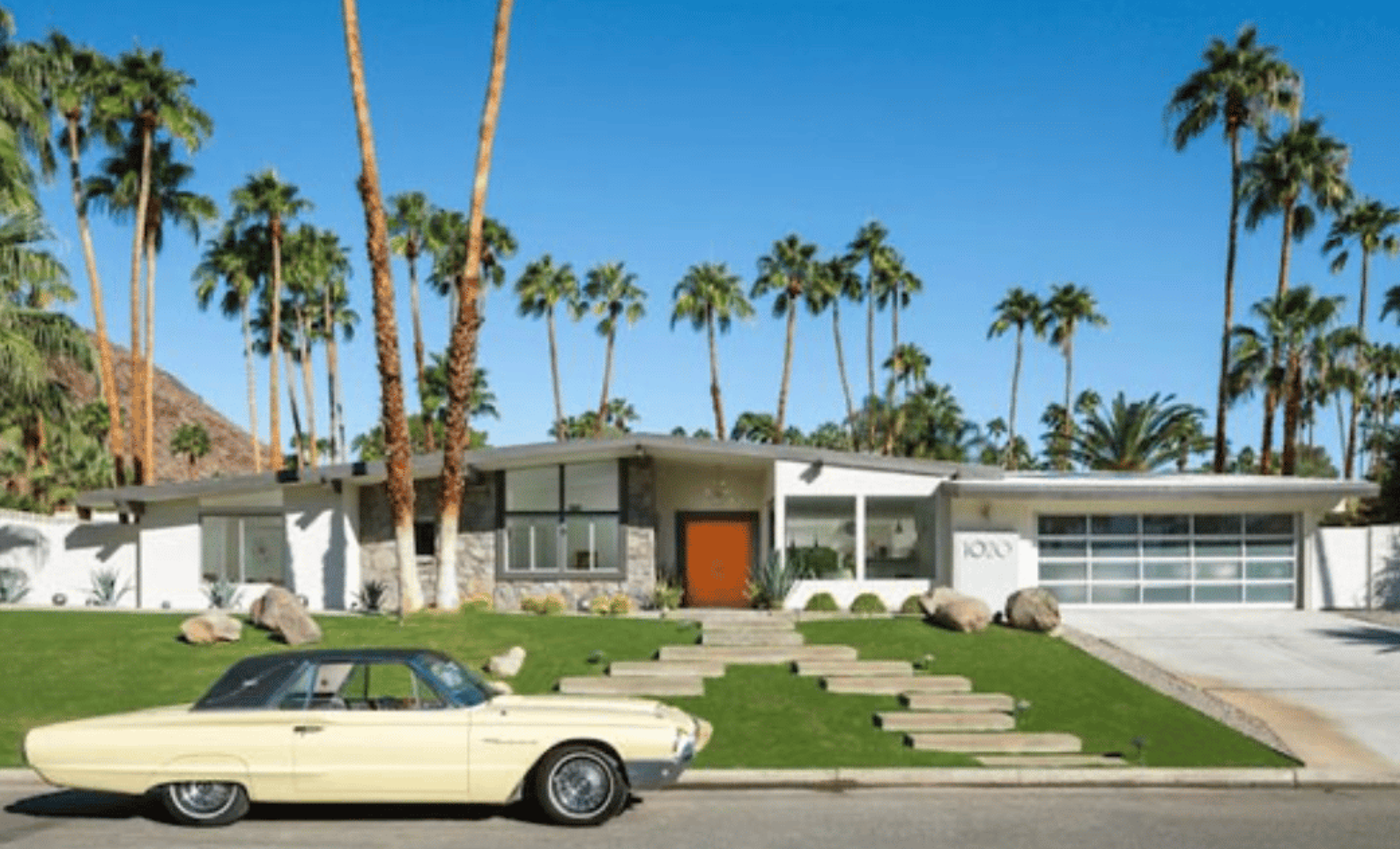 A mid-century modern house with a yellow classic car out front