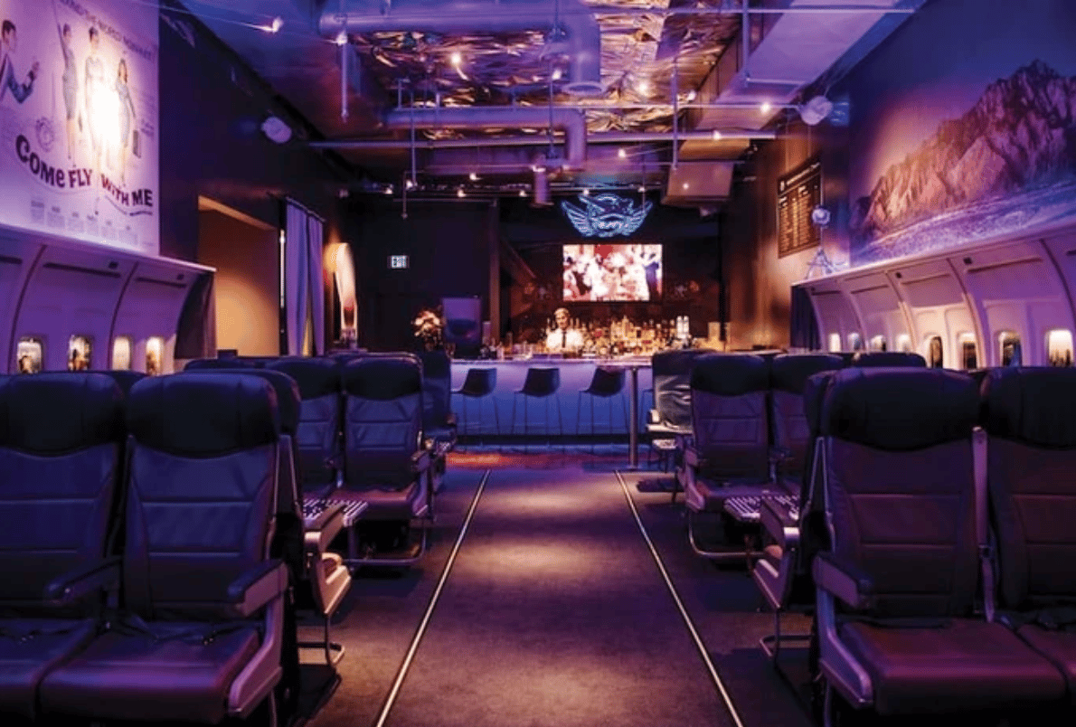 Interior of PS Air Bar with purple lighting, airplane seats, and a bar in the back