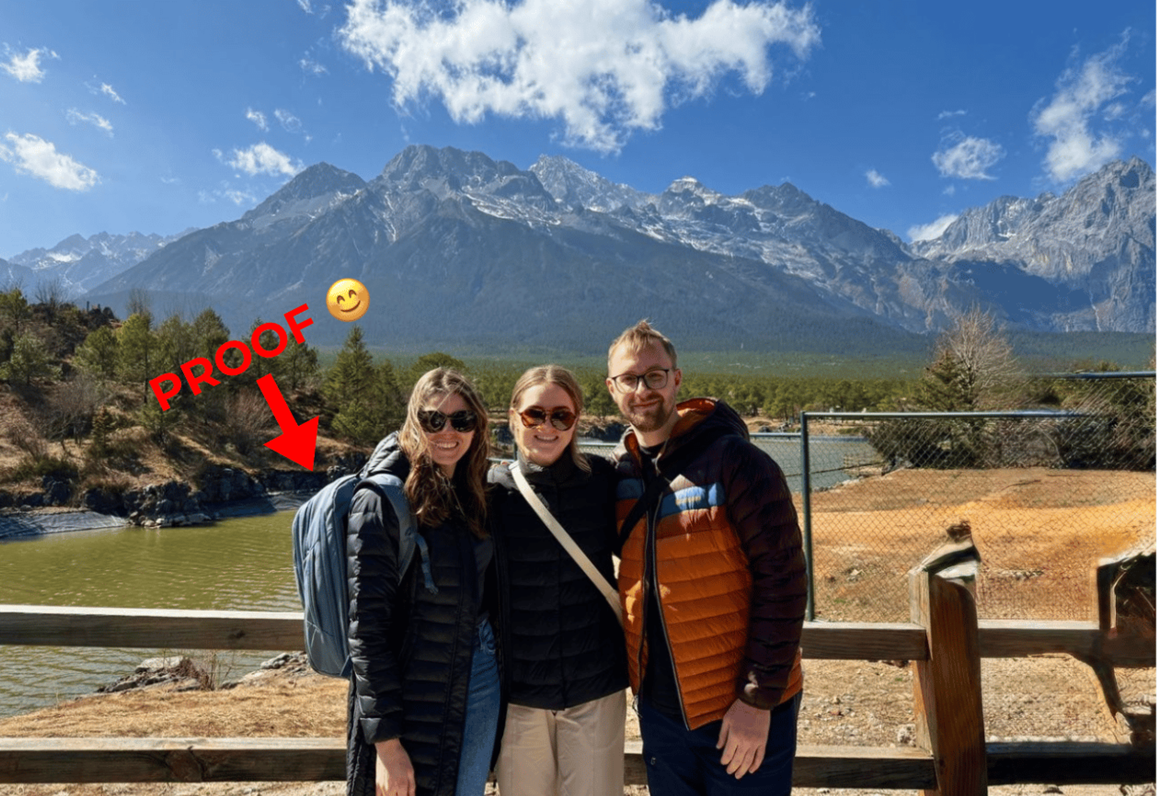 Three people standing in front of a fence and mountain