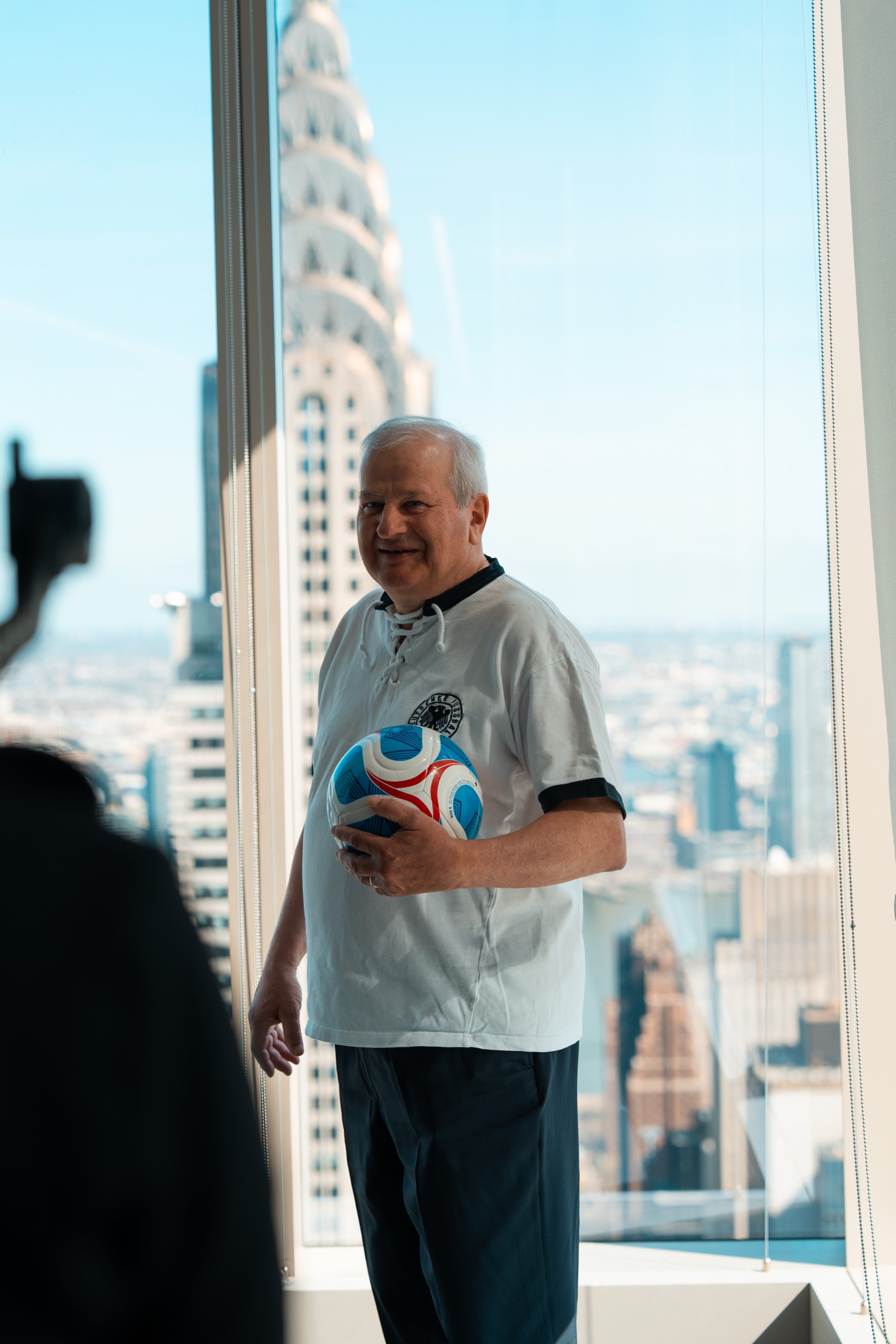 Guest in a Germany football shirt holding a ball by the window, Chrysler Building behind