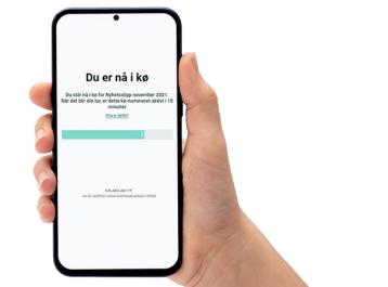 Hånd som holder telefon som viser hvor man er i den digitale køen.