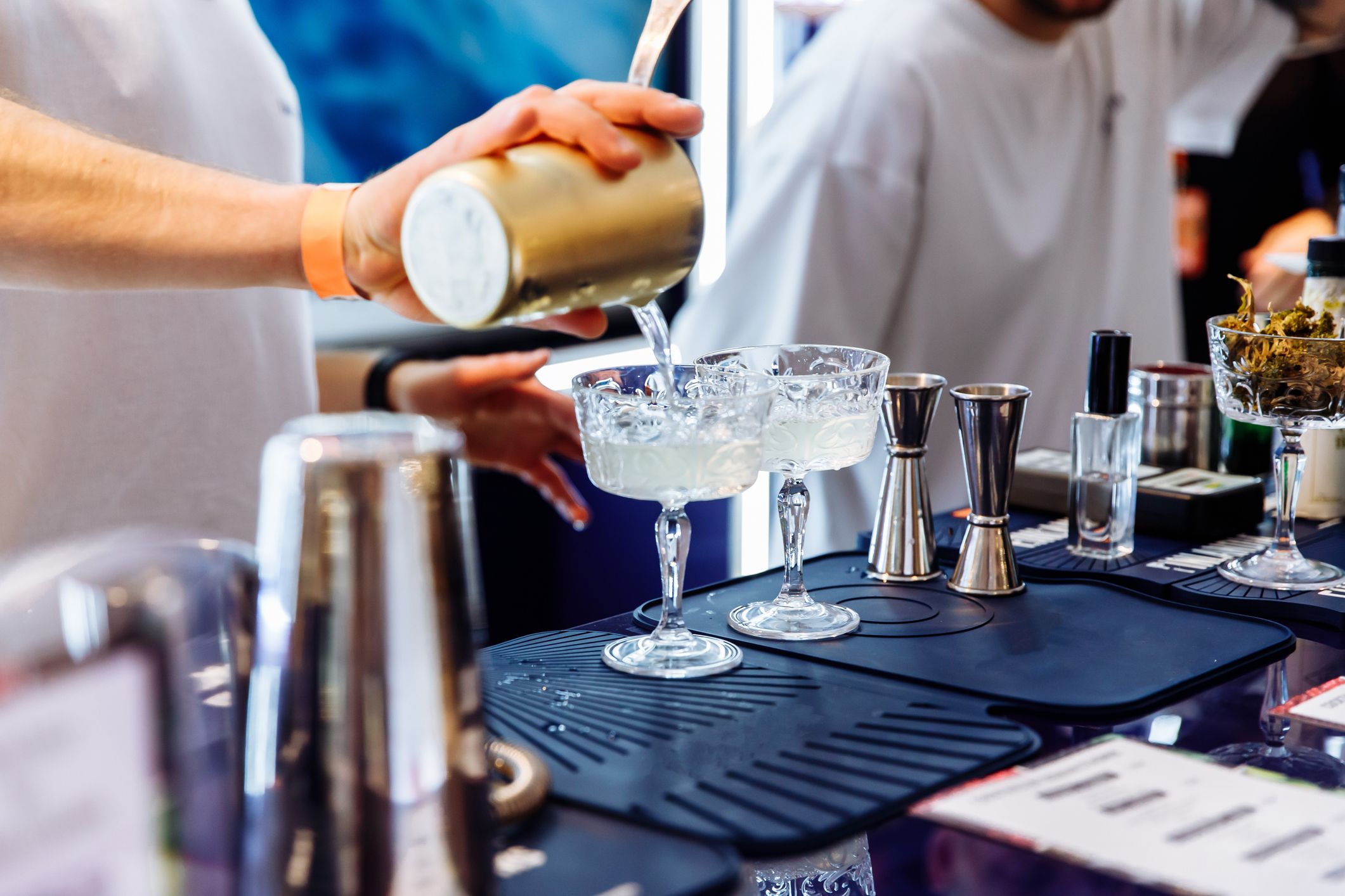 Bartender skjenker drinker i to cocktailer på en bardisk.