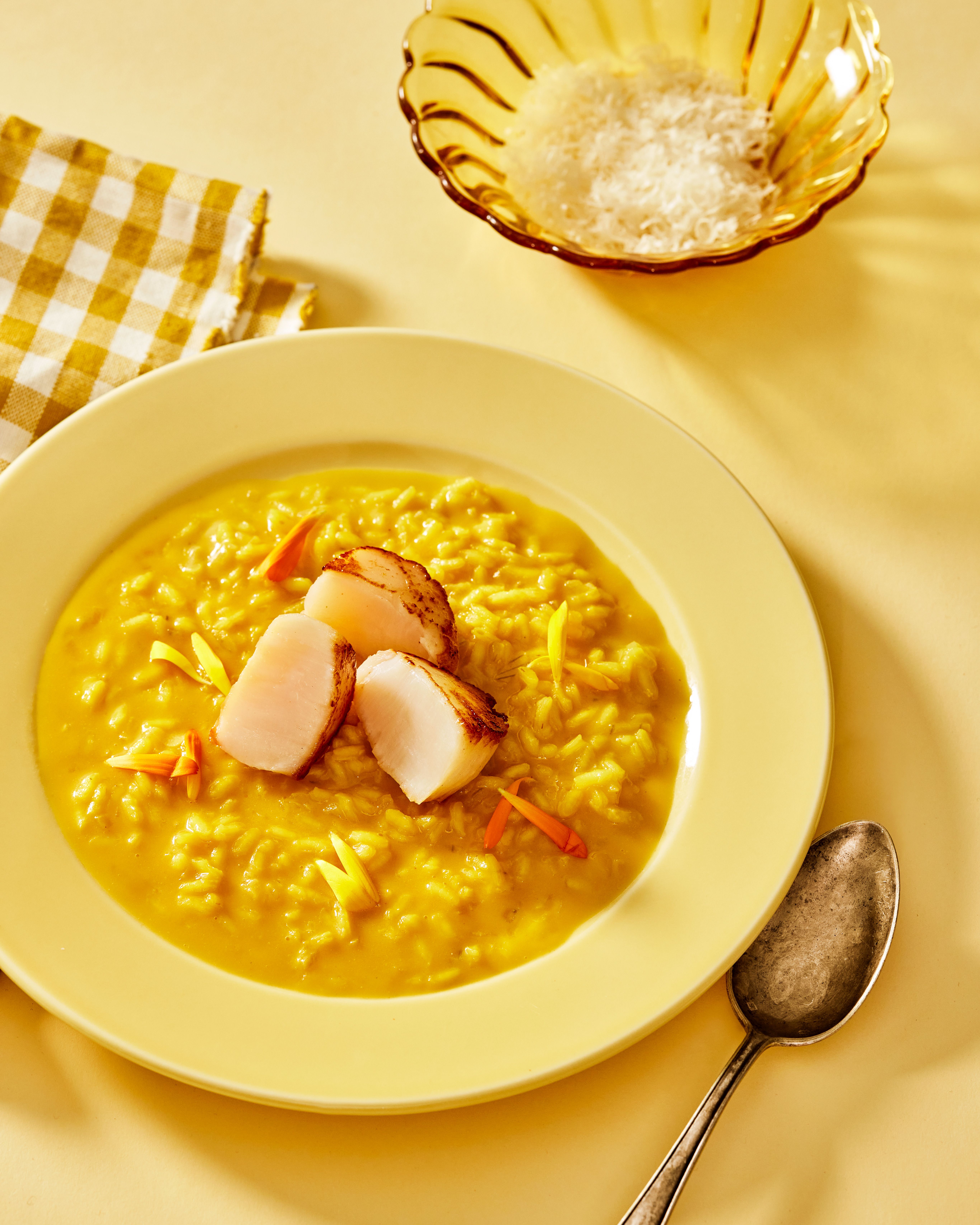 gult bord med serviett og tallerken med safranrisotto og stekte kamskjell.