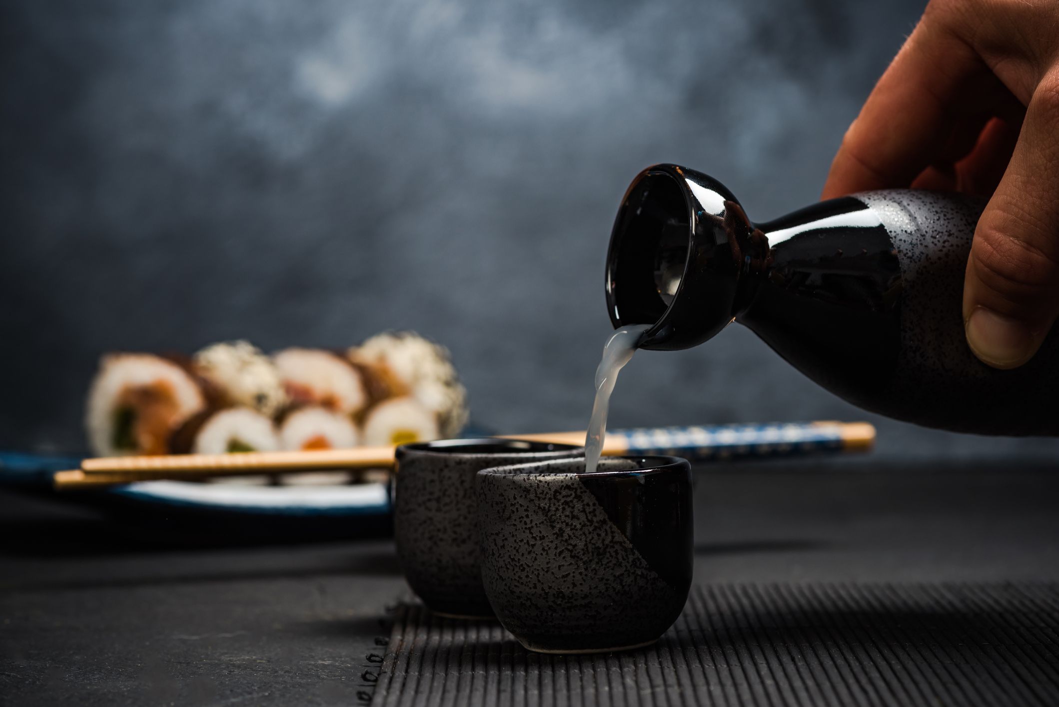 Sake helles i to små kopper med en tallerken med sushi bak.