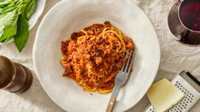 Tallerken med spaghetti bolognese, parmesan, basilikum og et glass rødvin.