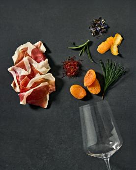 Spekeskinke, safran, tørket aprikos, te, appelsinskall, rosmarin og barnåler og et tomt vinglass.