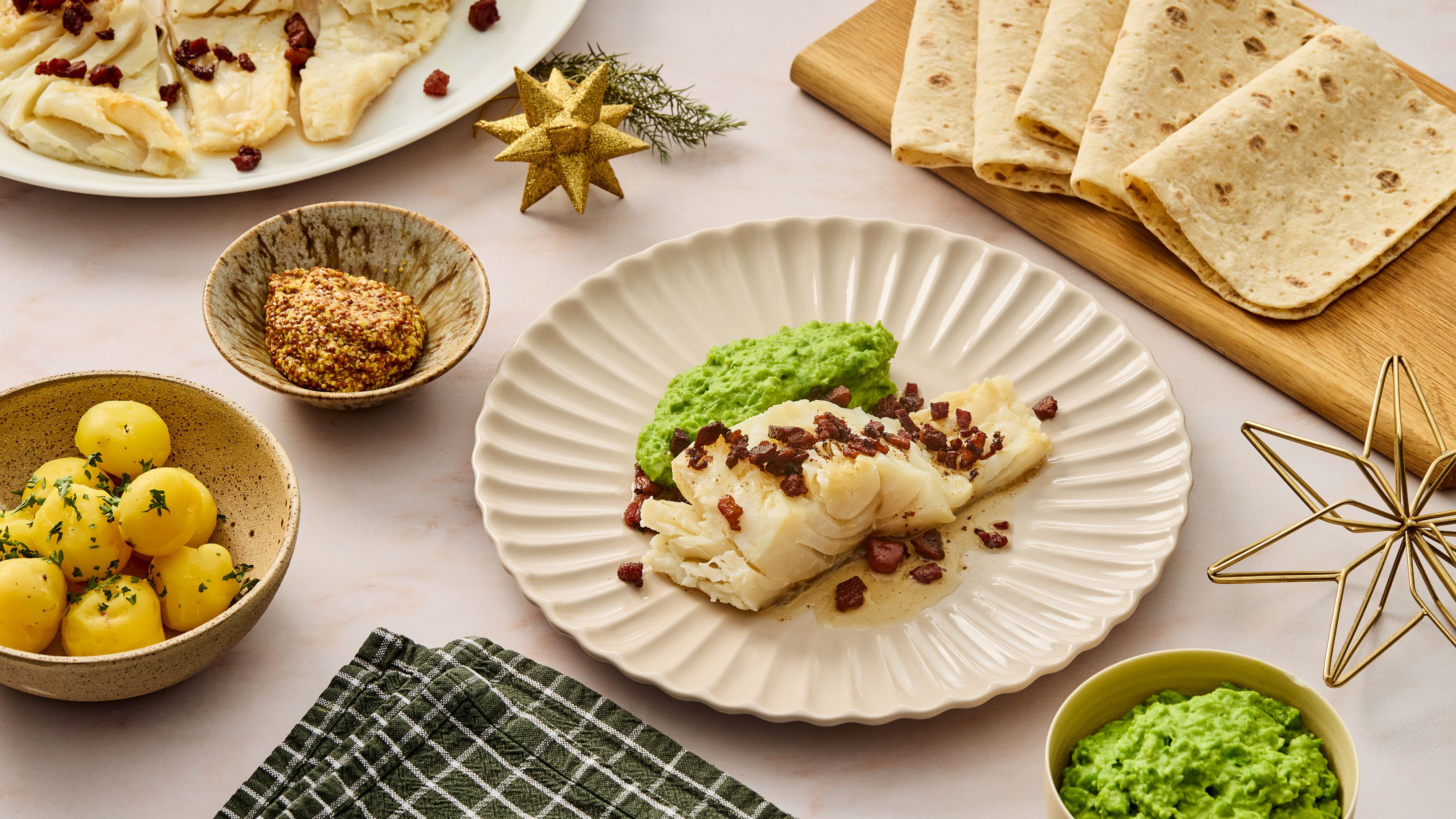 Tallerken med lutefisk, bacon og ertepuré. Fjøl med lefser og skåler med tilbehør.