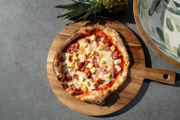 pizza med bacon og ananas på en trefjøl.