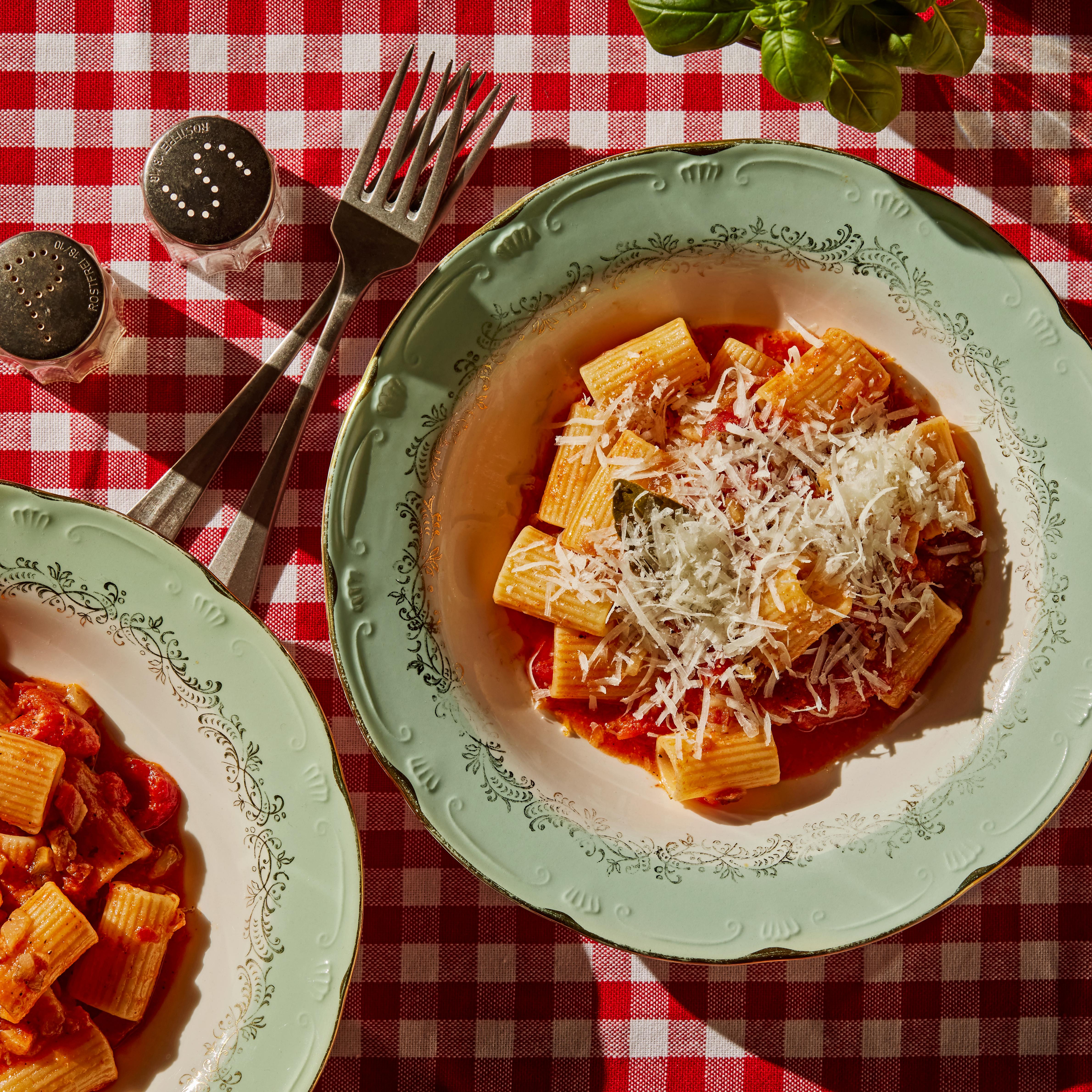 Tallerken på rød- og hvitrutete duk med pasta amatriciana med tomatsaus og guanciale og revet ost.