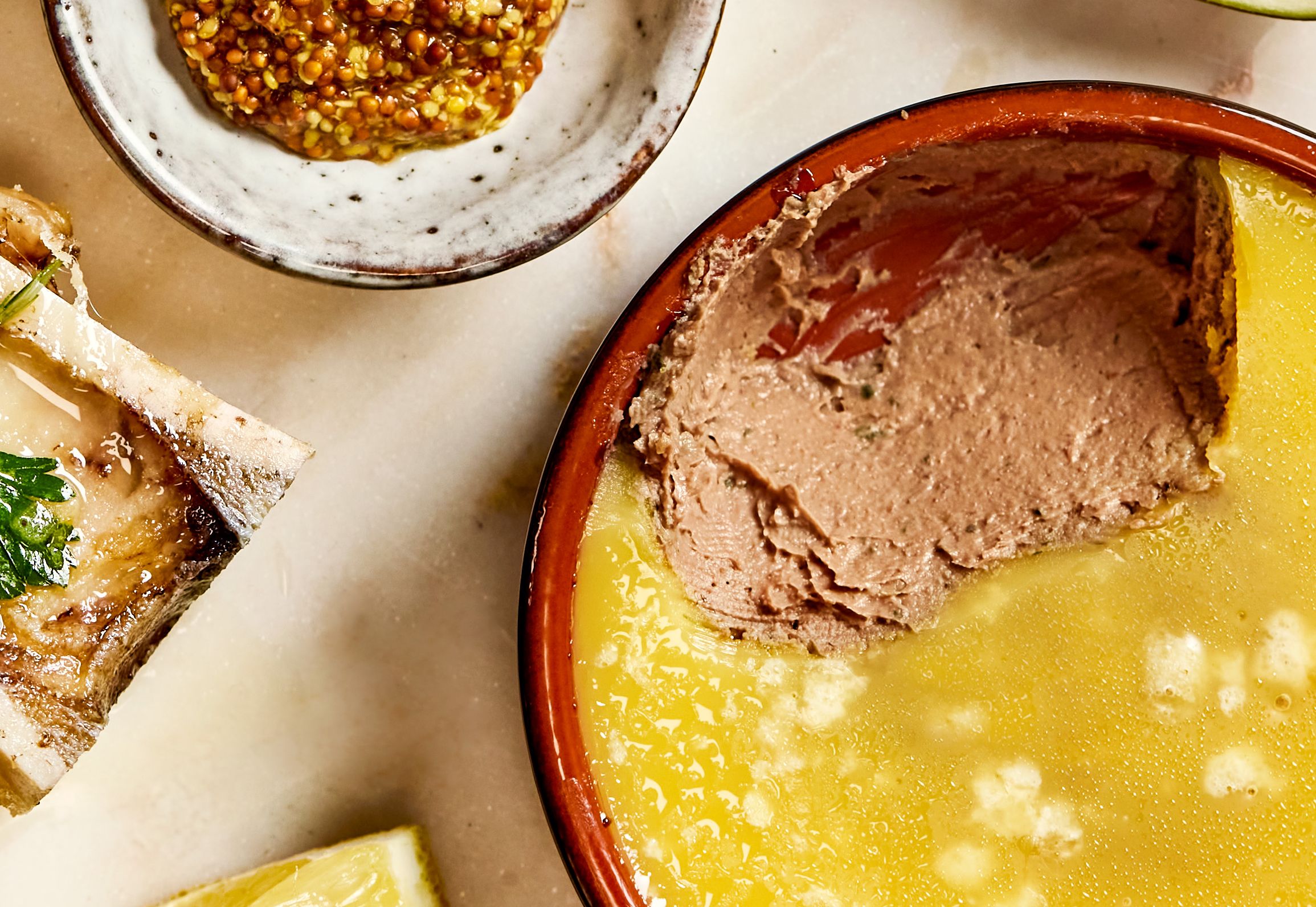 Gratinert margbein og kyllingleverterrine på et bord, skåler med toast, pickles, sennep og fersk fiken.