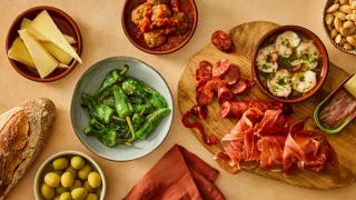Skåler og fat med tapas, som manchego, oliven, kjøttboller, chorizo, soekeskinke, pil pil, ansjos og mandler.