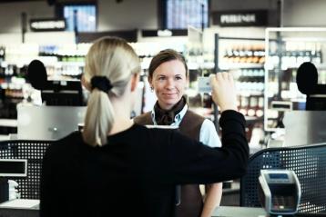 Ung kvinner viser legitimasjon til butikkekspeditør i kassen.